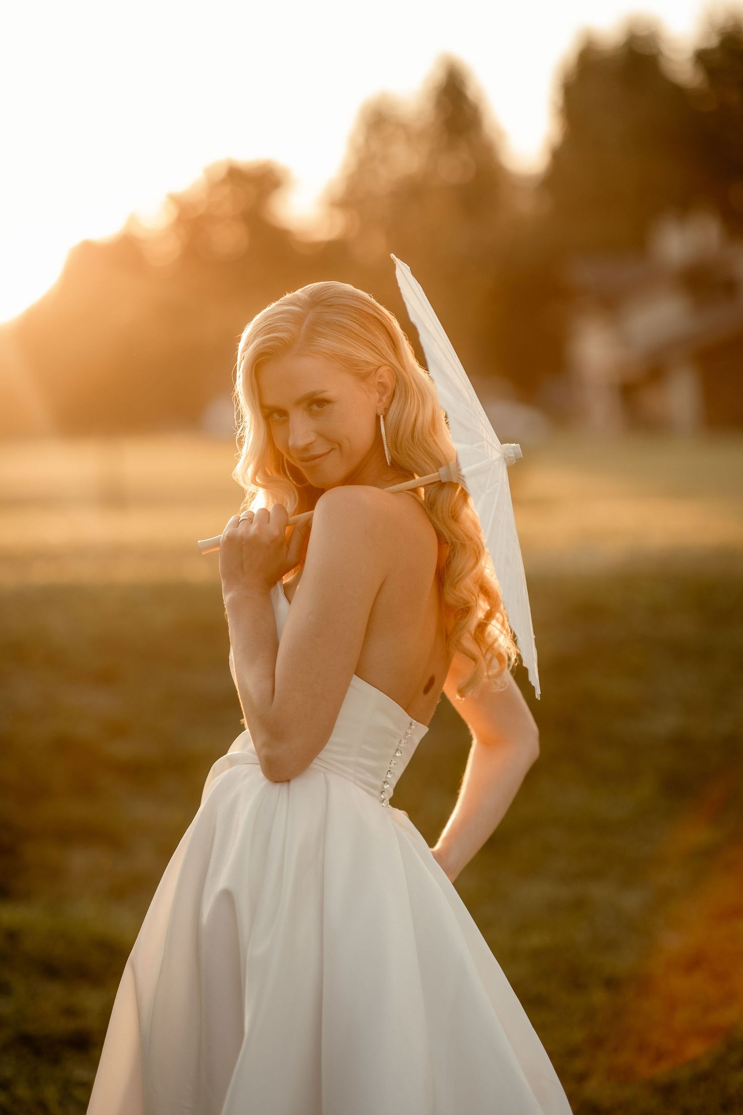 A bride in a white strapless wedding gown poses outdoors during golden hour sunset lighting.