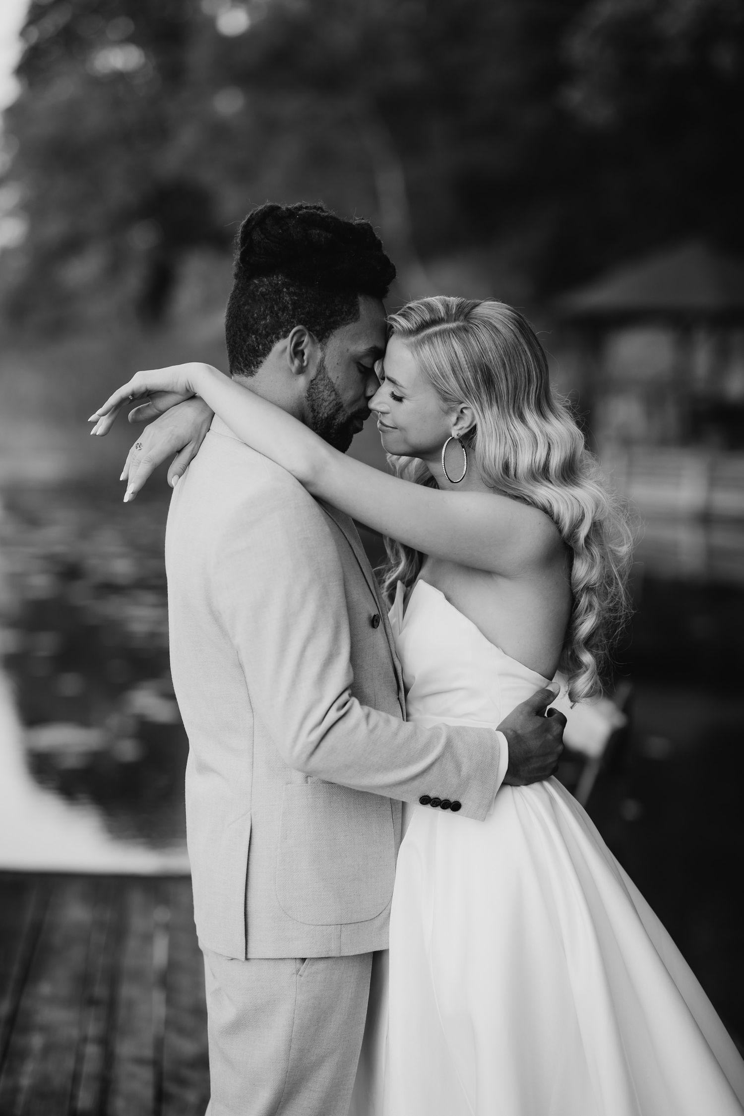 A romantic black and white wedding photo showing a couple embracing in a tender moment by a lake.