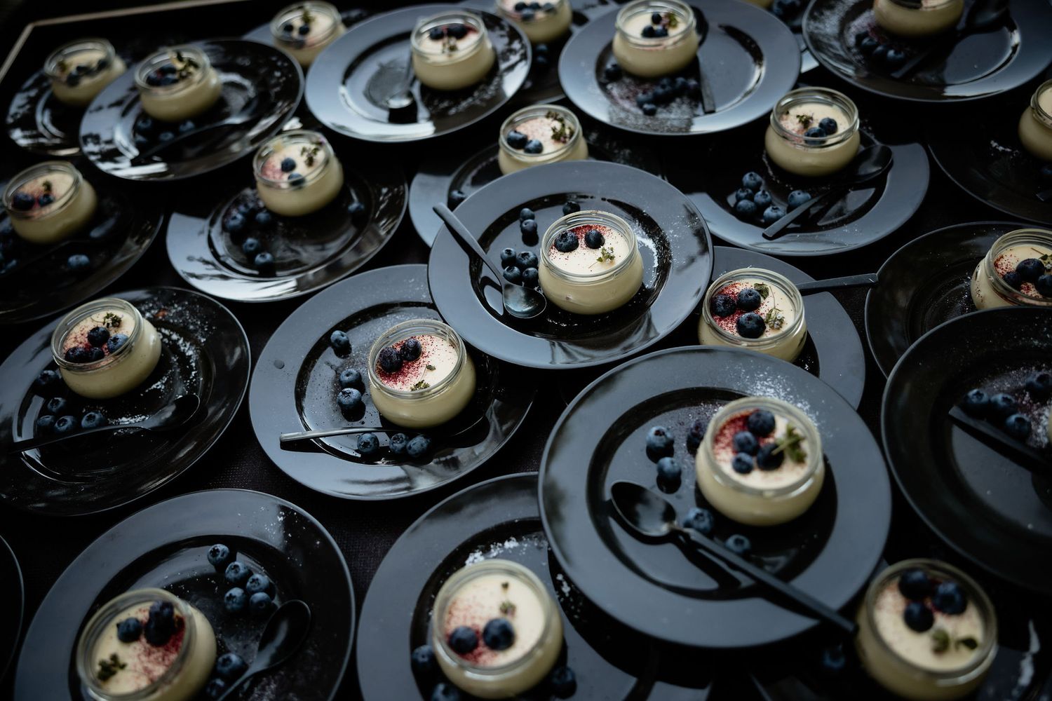 Artistic display of black plated desserts with cream and berry toppings.