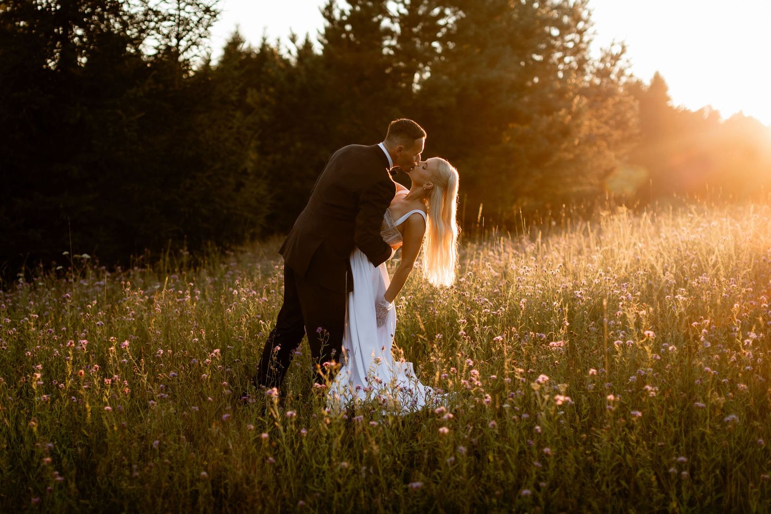Bride and groom share a romantic moment in a wildflower field at sunset.