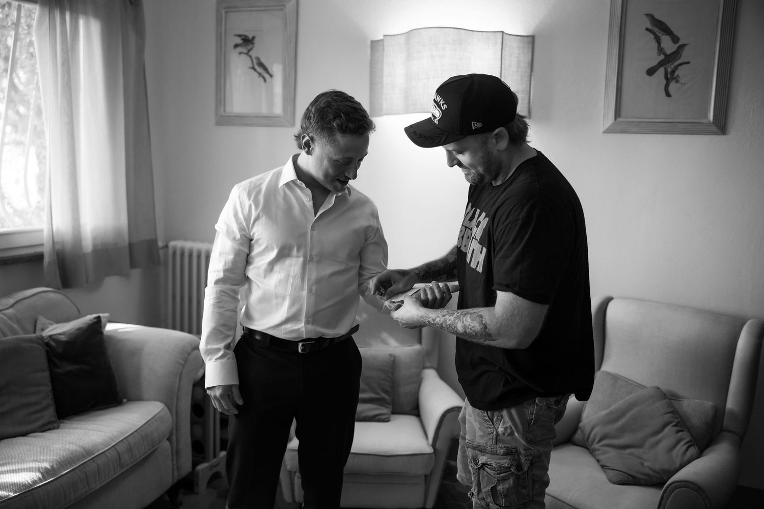 Two people in a room having a conversation, with one wearing a white shirt and another in a black hat and t-shirt.