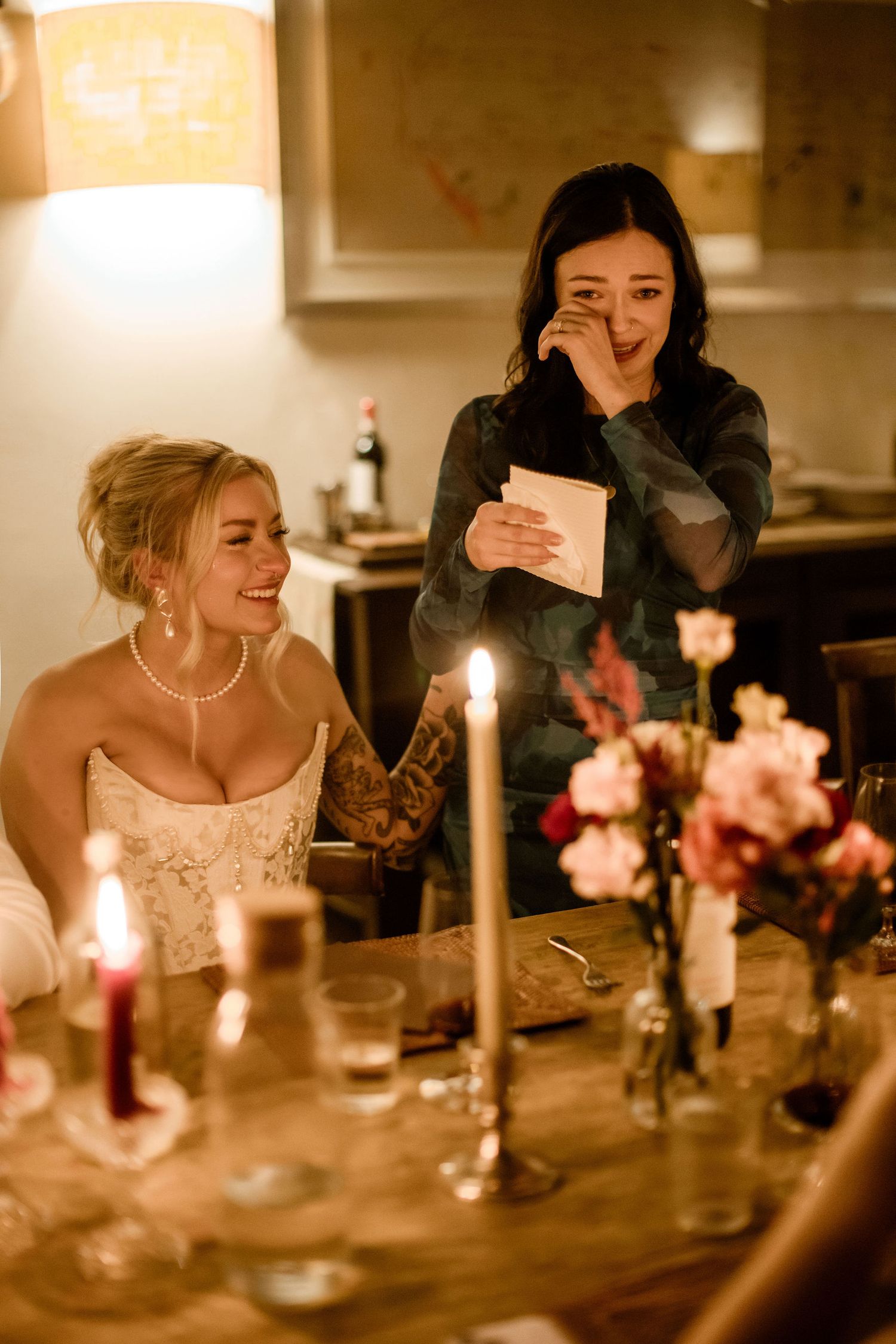 A candlelit dinner table with soft lighting and pink floral arrangements creates an intimate, romantic atmosphere.