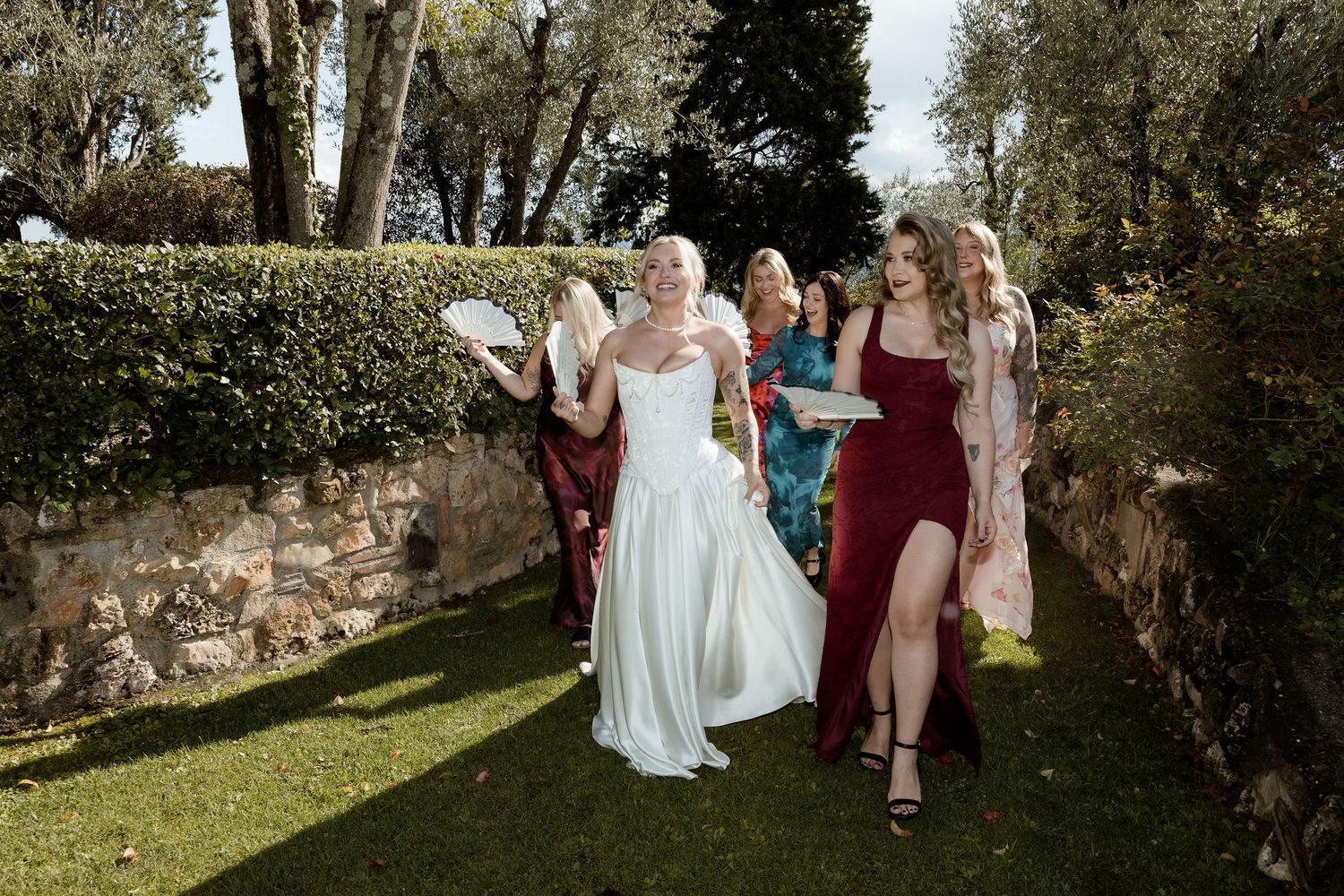 A group of wedding guests and bridal party members walk along a garden path during an outdoor celebration.