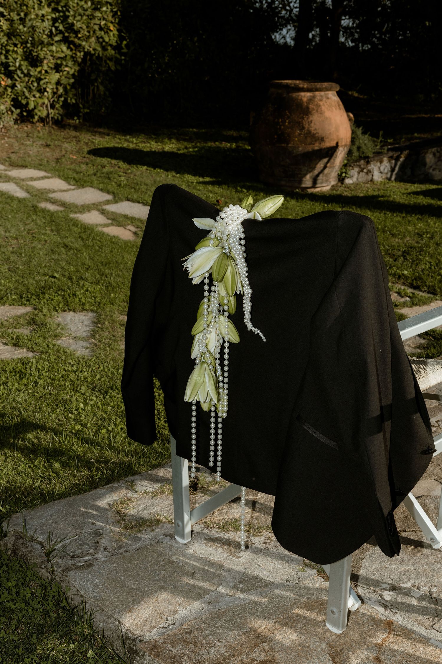 A black shawl draped over a chair with white floral decorations and pearls in an outdoor garden setting.