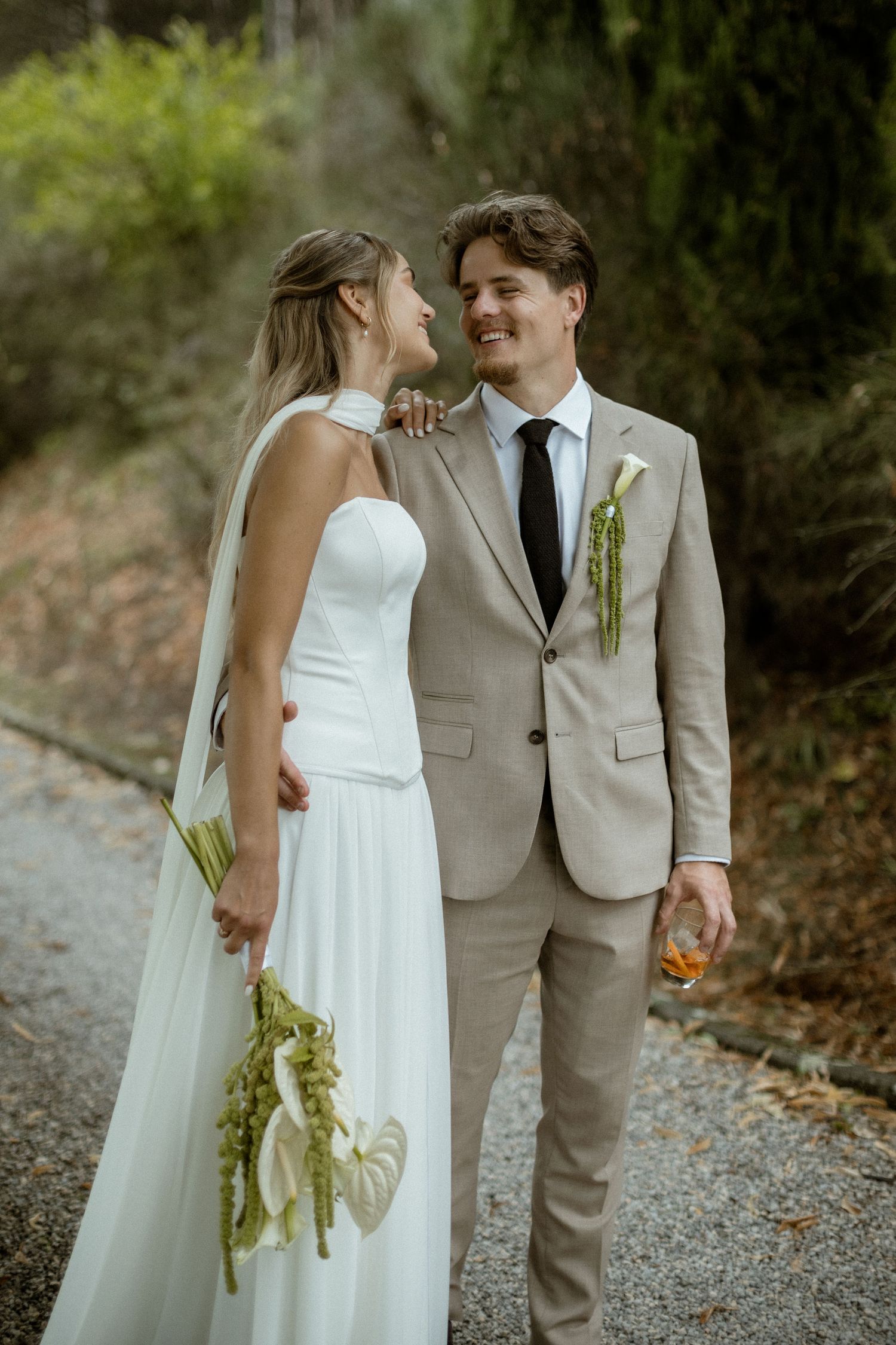 A romantic wedding couple shares intimate moments on a gravel path surrounded by lush greenery.