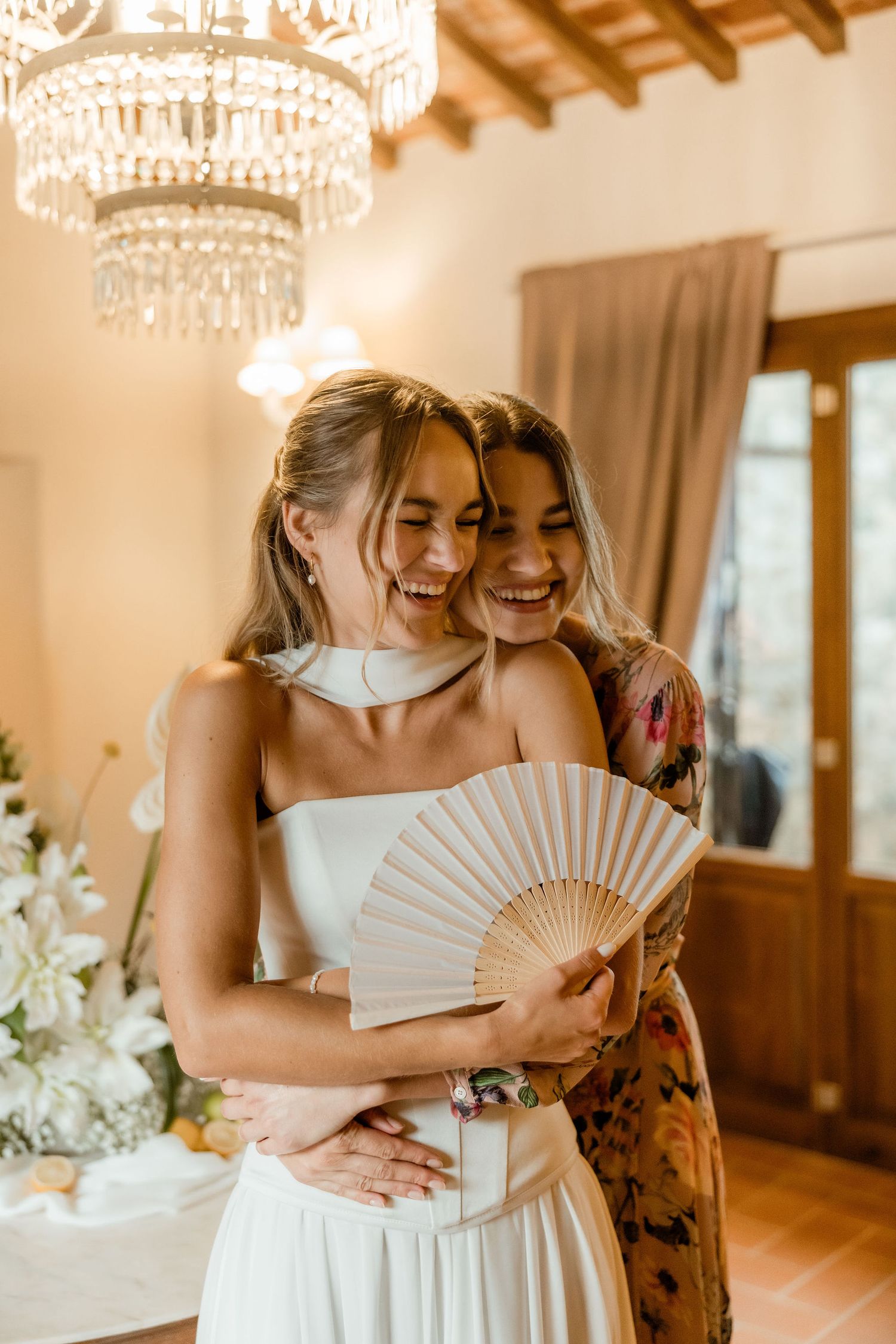 Three similar photos show two people embracing and laughing while holding white paper fans in an elegant indoor setting.