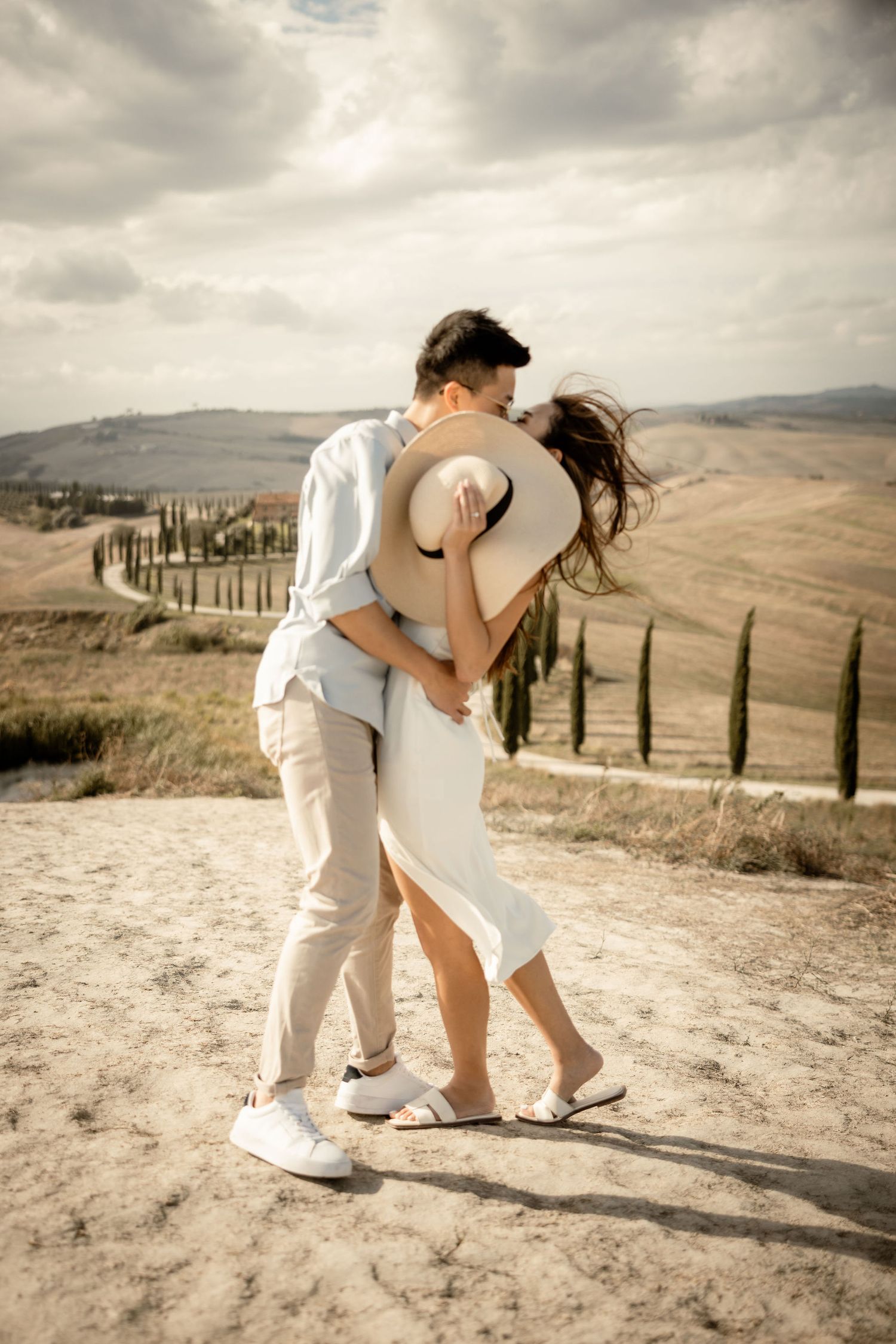 Couple in light colored outfits dancing on a hilltop overlooking a scenic Tuscan landscape.