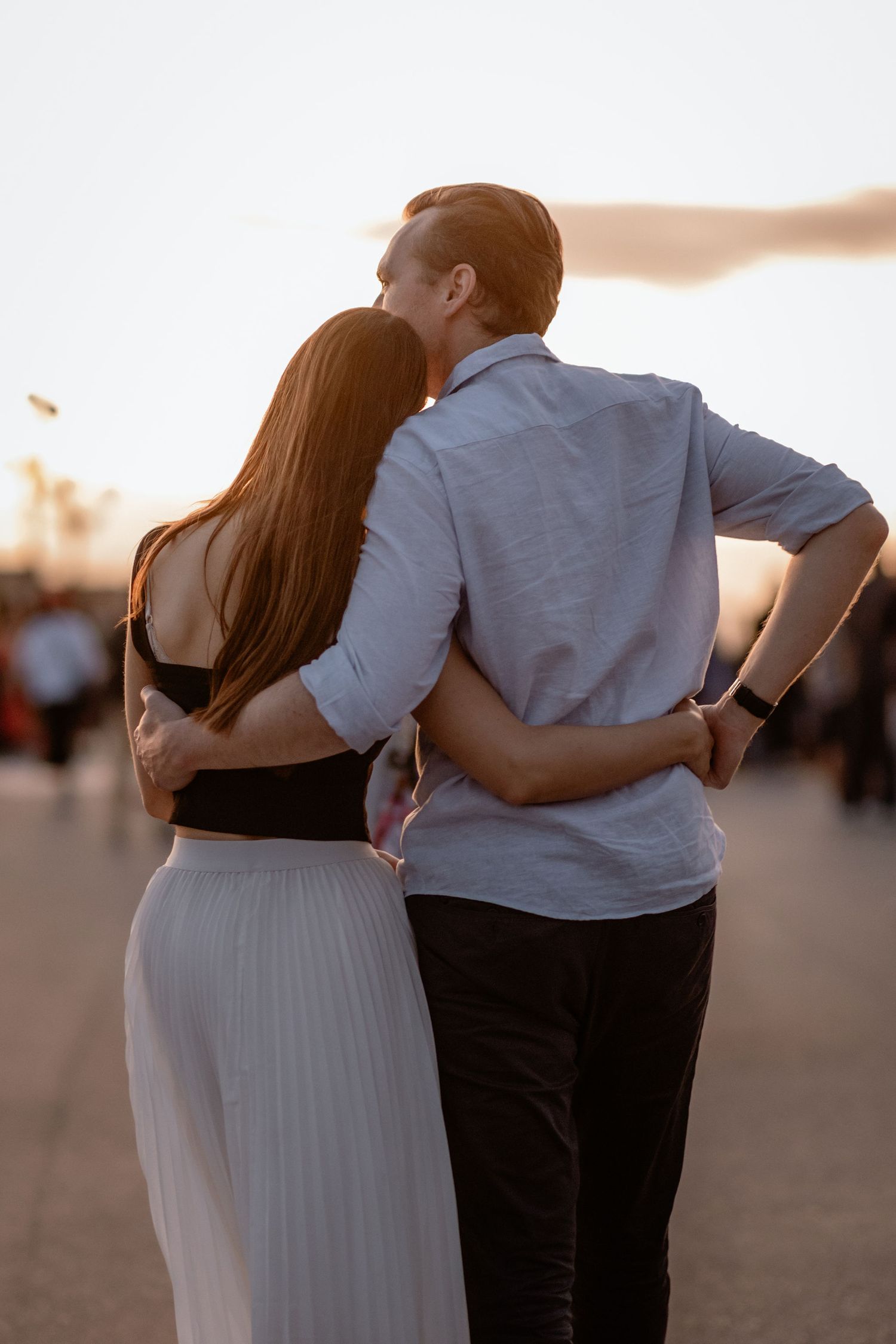 A couple in casual attire embraces while watching the sunset together outdoors on a warm evening.