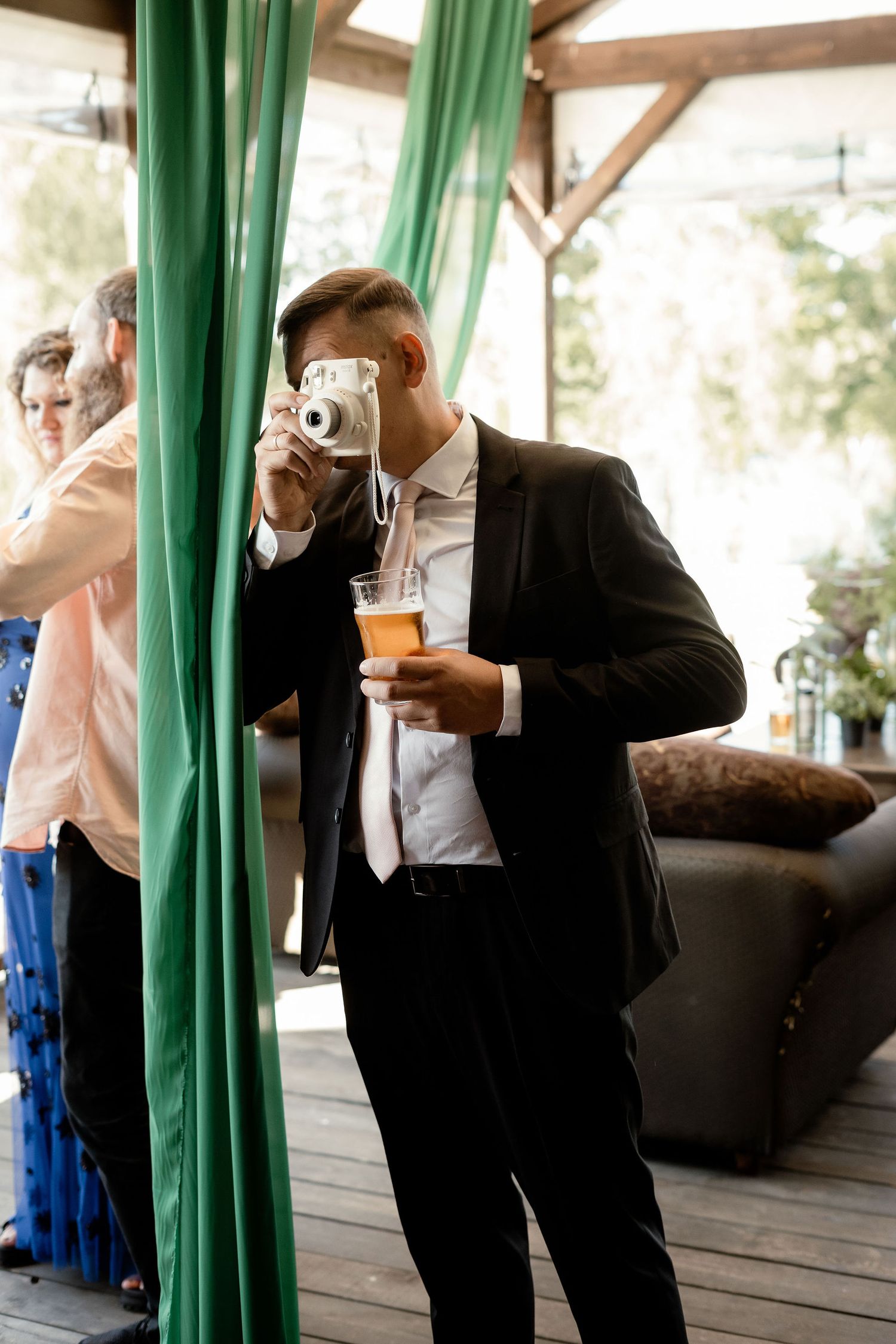 Guest taking photos at wedding reception with vintage camera while holding a drink.