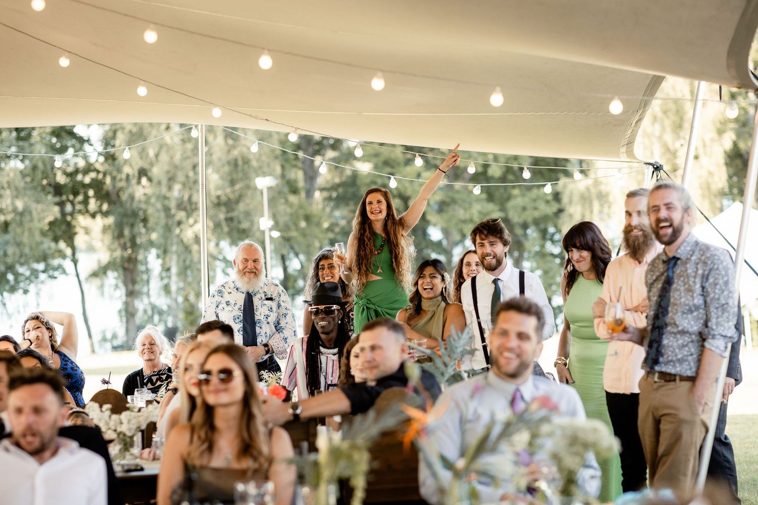 Wedding guests gathered under a tent for an outdoor reception celebration.