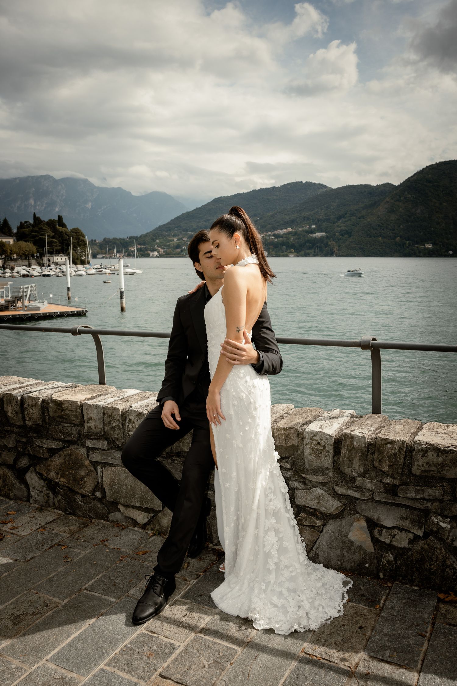 Romantic lakeside wedding portrait with mountain and marina backdrop.