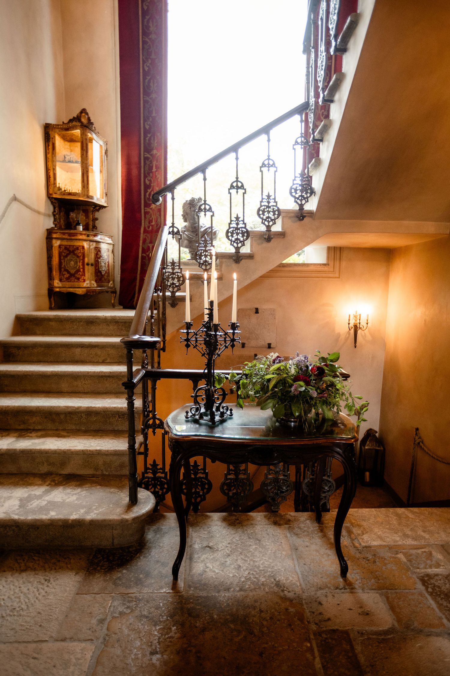 Elegant staircase with vintage lanterns and wrought iron details features an antique table with potted plants.
