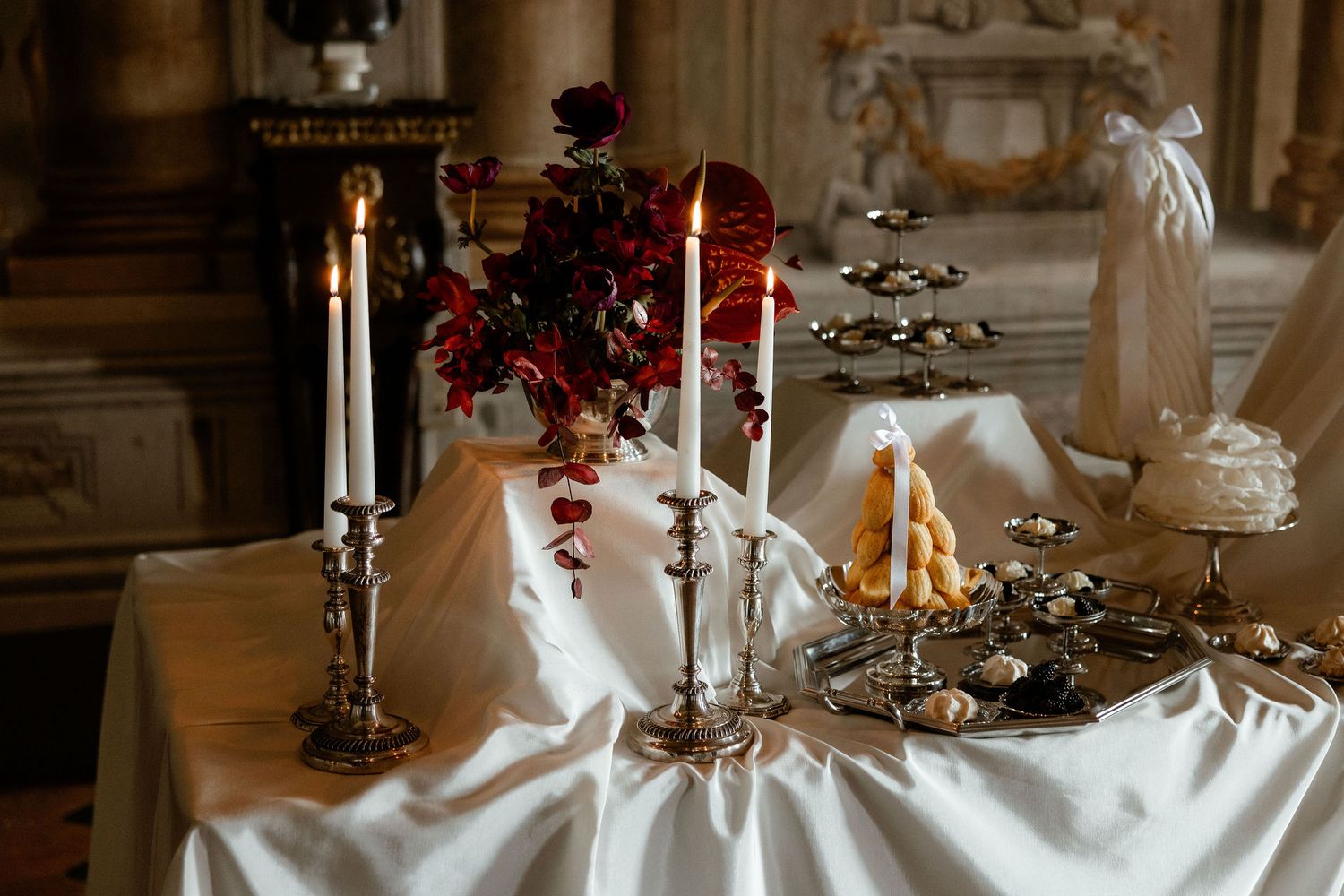 Elegant table setting with white linens, burgundy flowers and silver candelabras in a vintage interior.