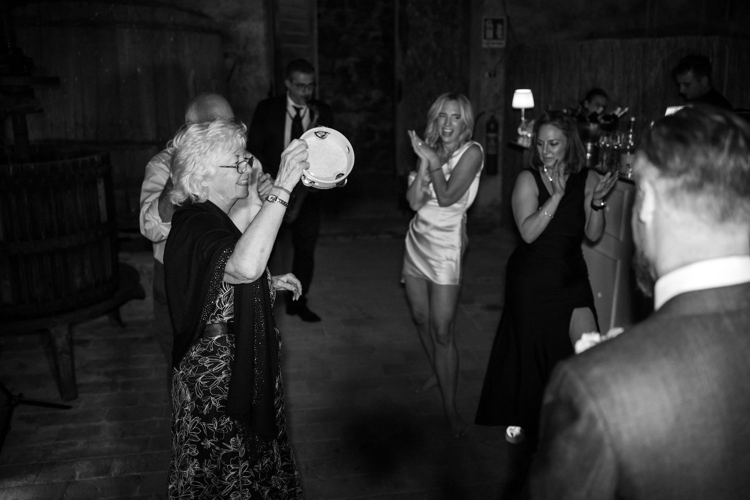 A group of people dancing and celebrating at a wedding reception in a dimly lit venue.