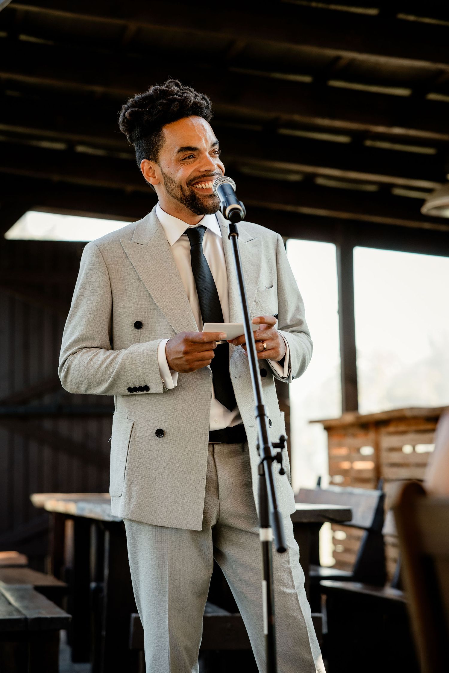 Speaker in light gray suit gives a speech at indoor wedding venue.