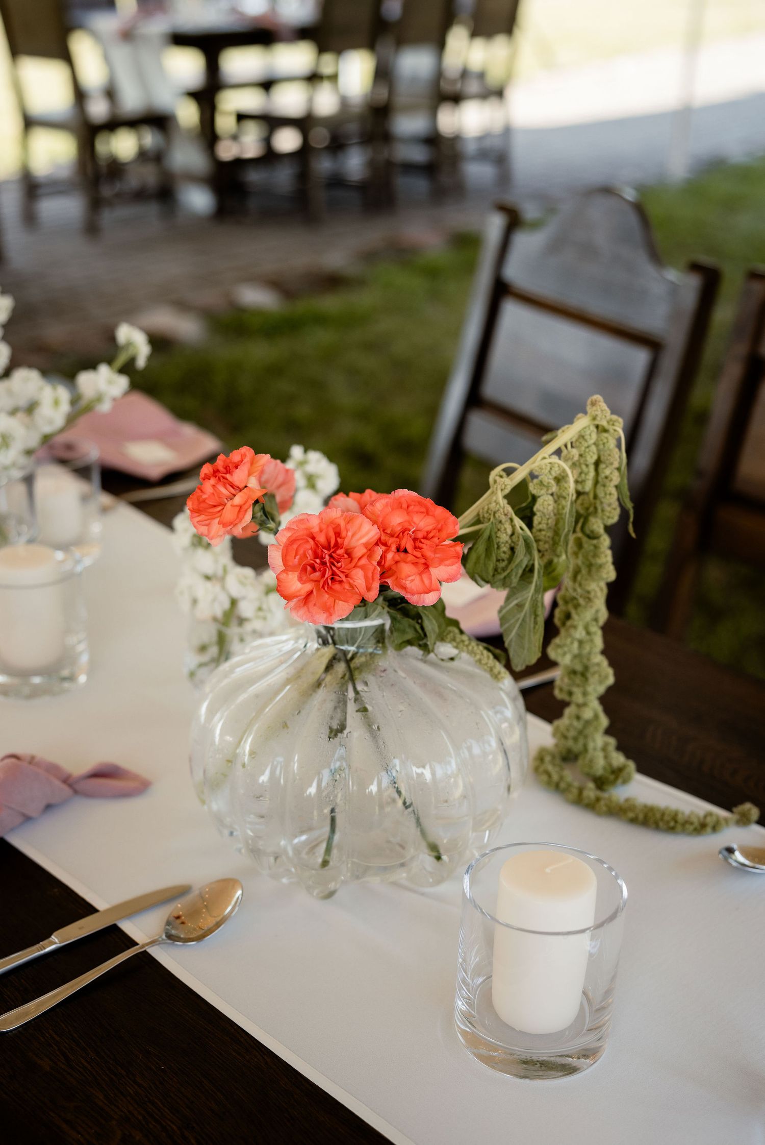 Elegant table setting with coral carnations in glass vase and white candle centerpieces.