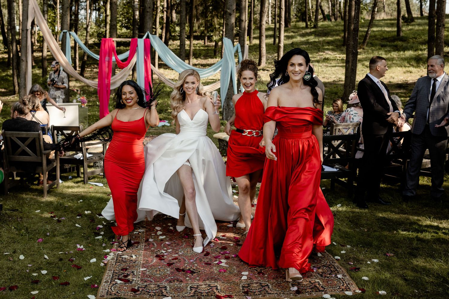 A celebratory moment at a wedding with red dresses and decorative drapes in a forest setting.