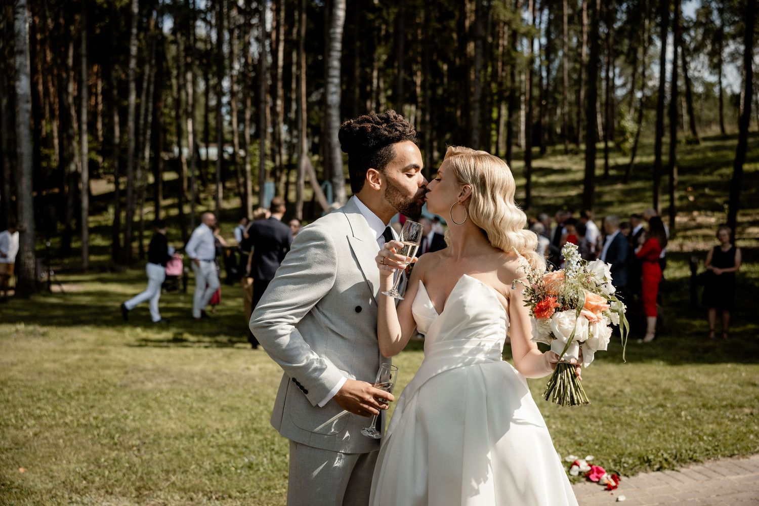Sunny outdoor forest wedding celebration with light gray suit and white gown.