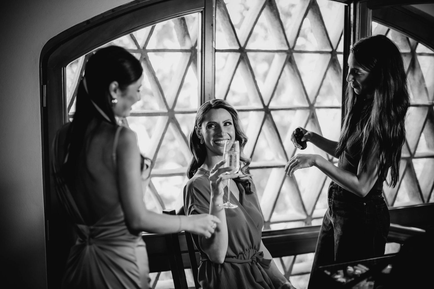 Black and white photo of wedding preparation scene by diamond-paned window.