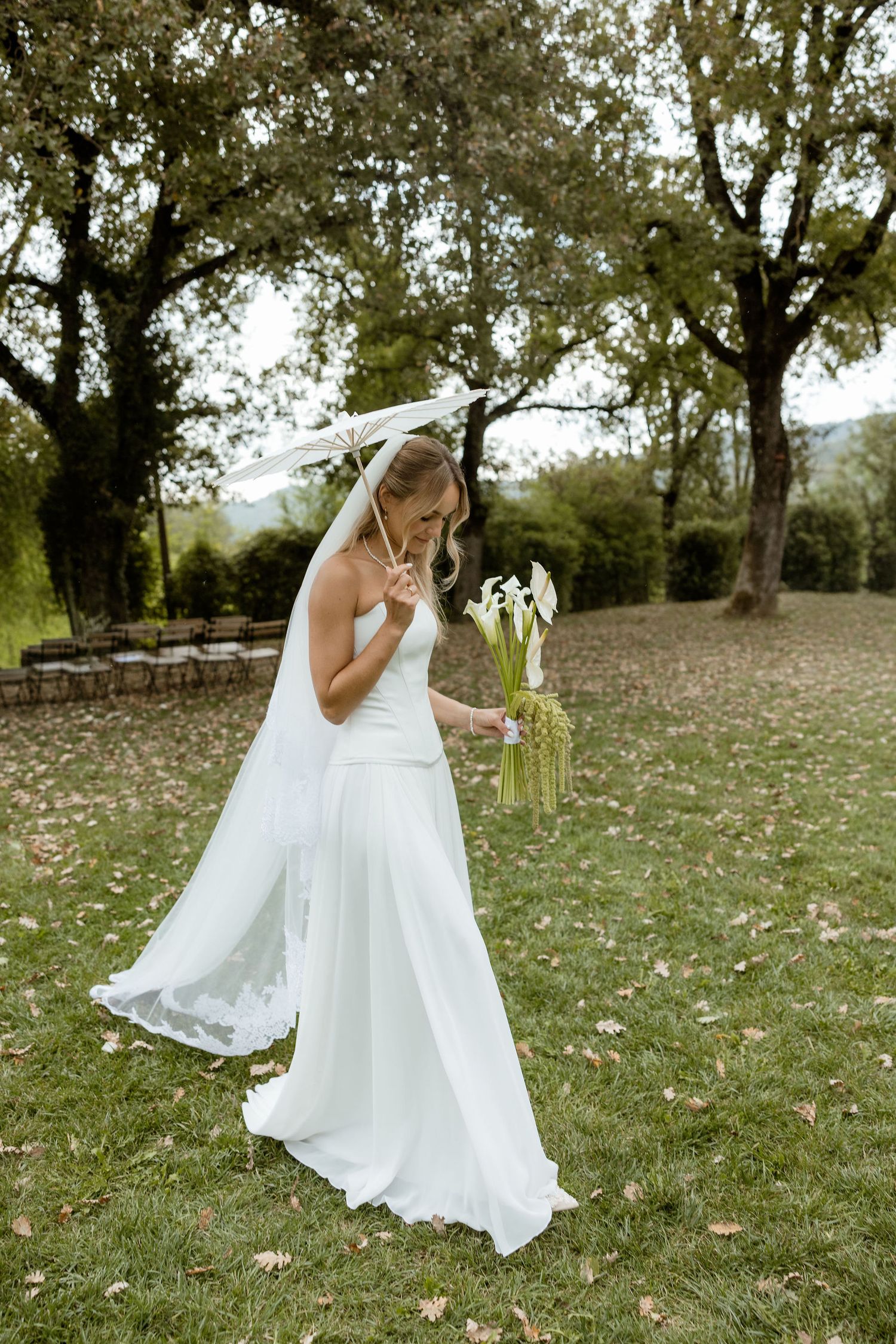 A flowing white wedding dress twirls gracefully in a meadow with scattered autumn leaves and trees in the background.