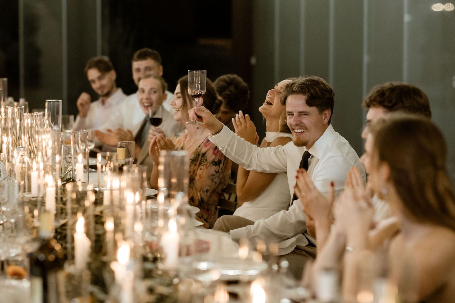 Wedding guests raise their glasses for a candlelit dinner toast at an elegant reception table.
