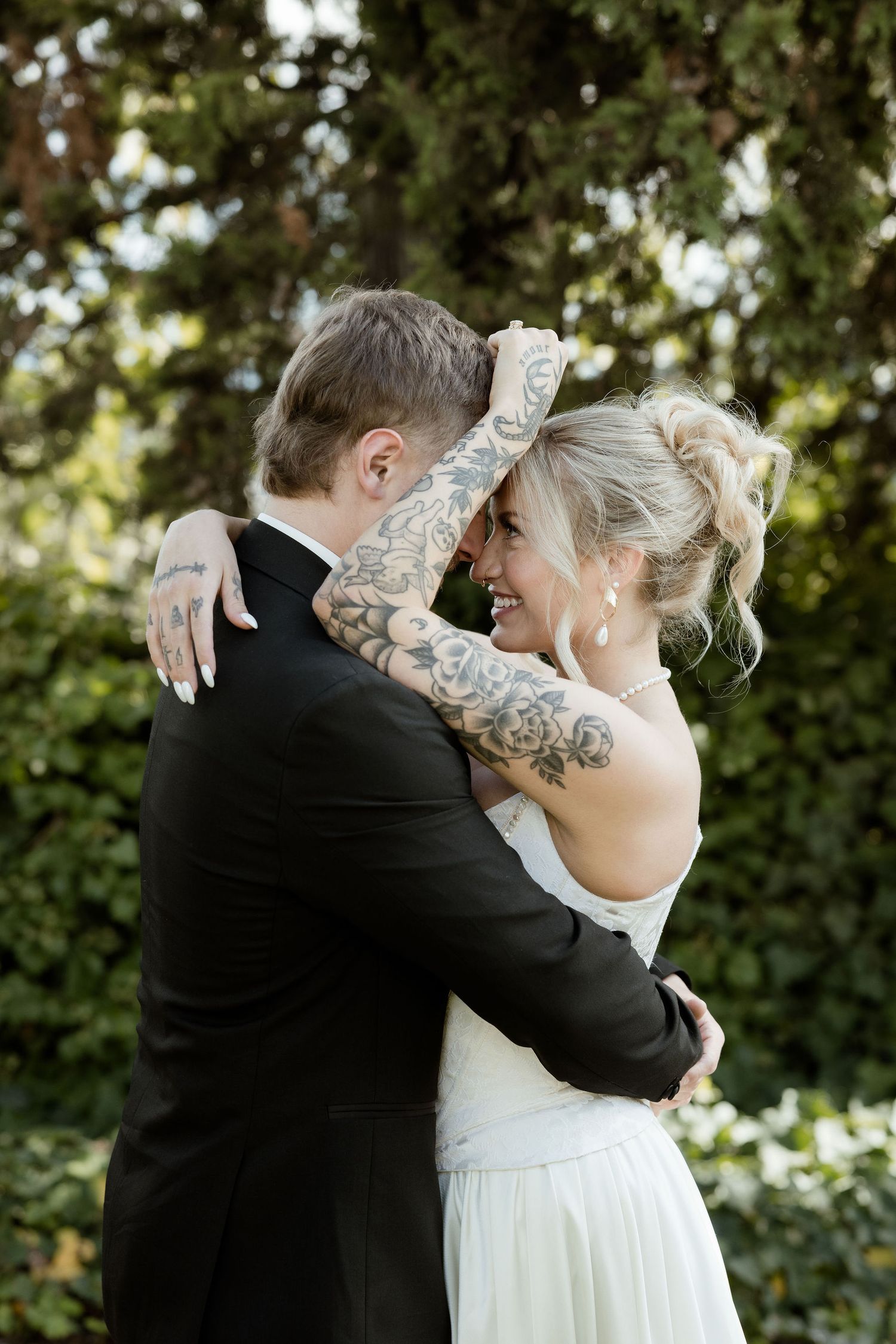 A couple shares a romantic moment in their wedding attire against a lush green garden backdrop.