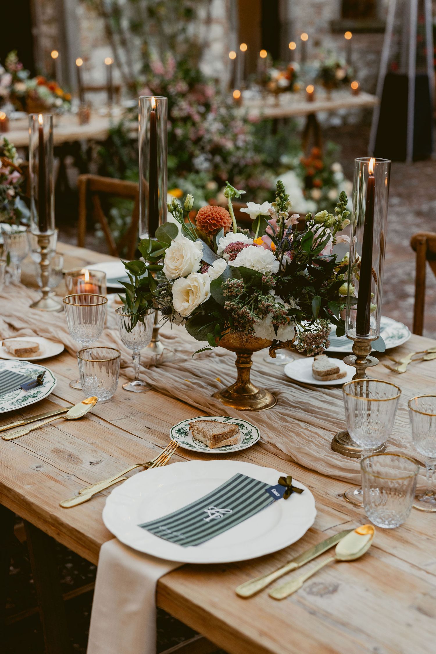 Elegant rustic wedding table setting with white flowers, tall black candles and vintage glassware on wooden farmhouse table.