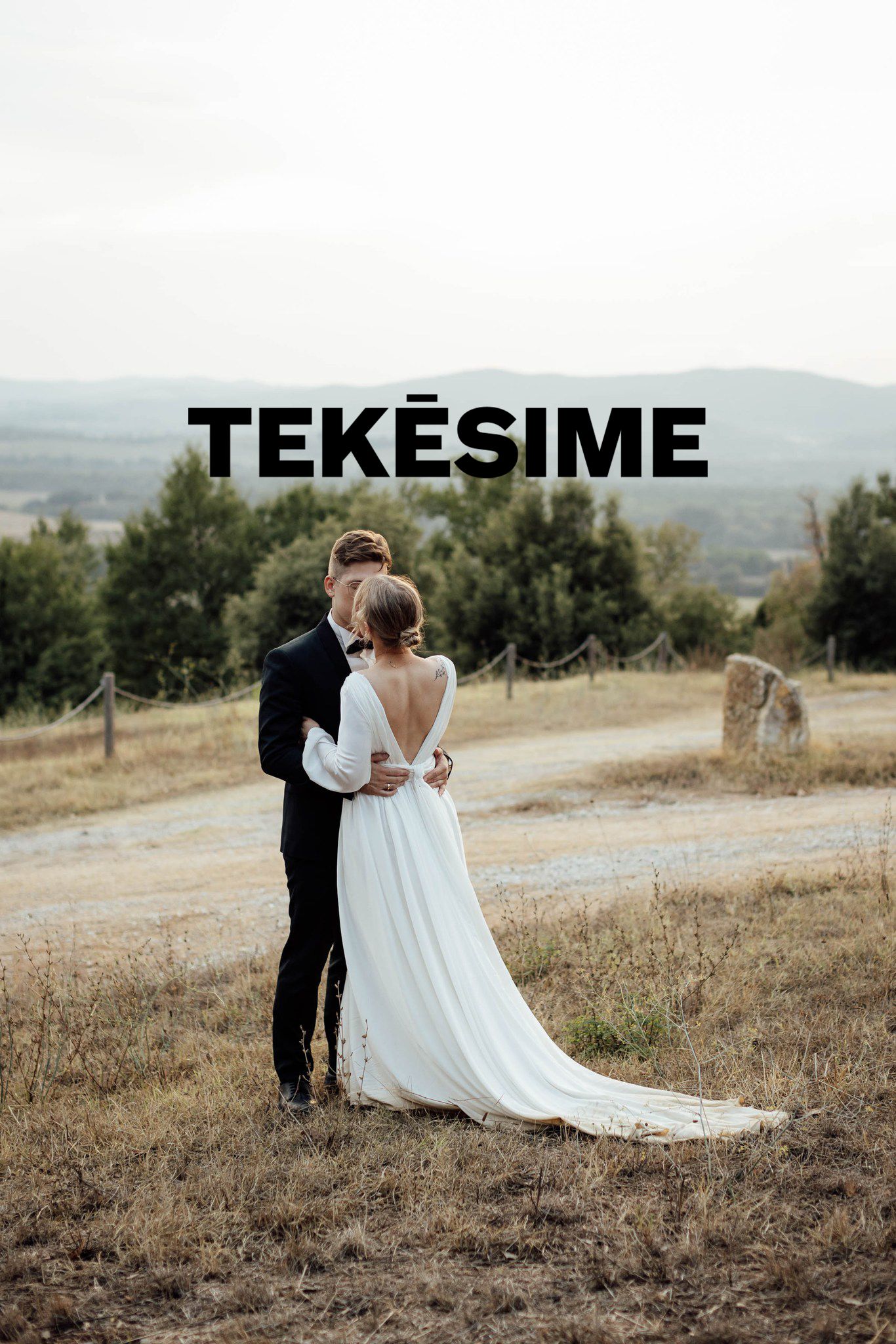 A couple in wedding attire embraces on a hilltop meadow with mountains in the background during golden hour.