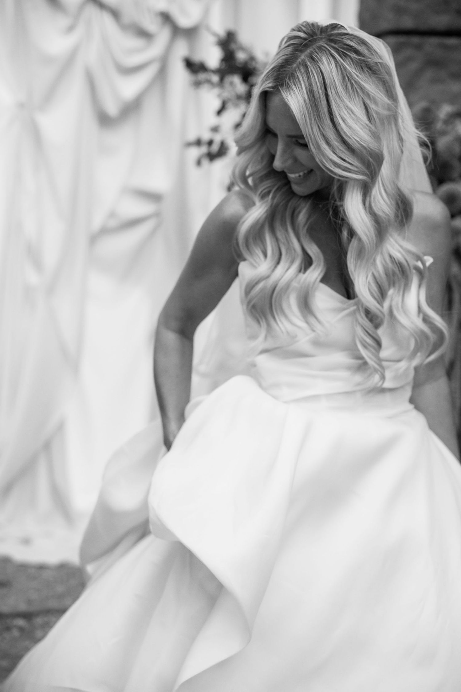 A series of black and white photos showing details of a bride's elegant white wedding dress with ruffles and flowing fabric.
