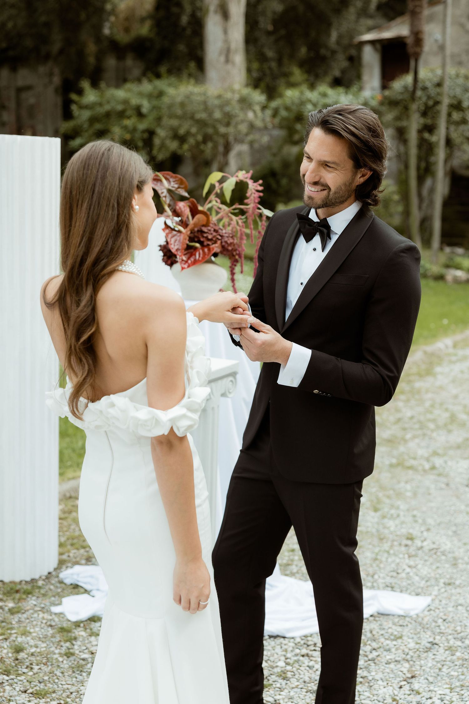 A romantic wedding moment on a gravel path, with the bride in white and groom in a classic black tuxedo and bow tie.