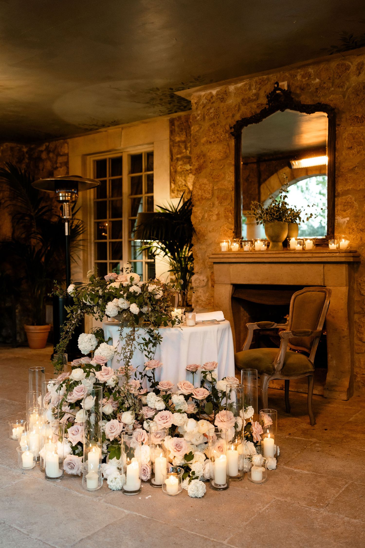 Romantic candlelit wedding reception setup with white floral arrangements and French doors in a rustic stone room.