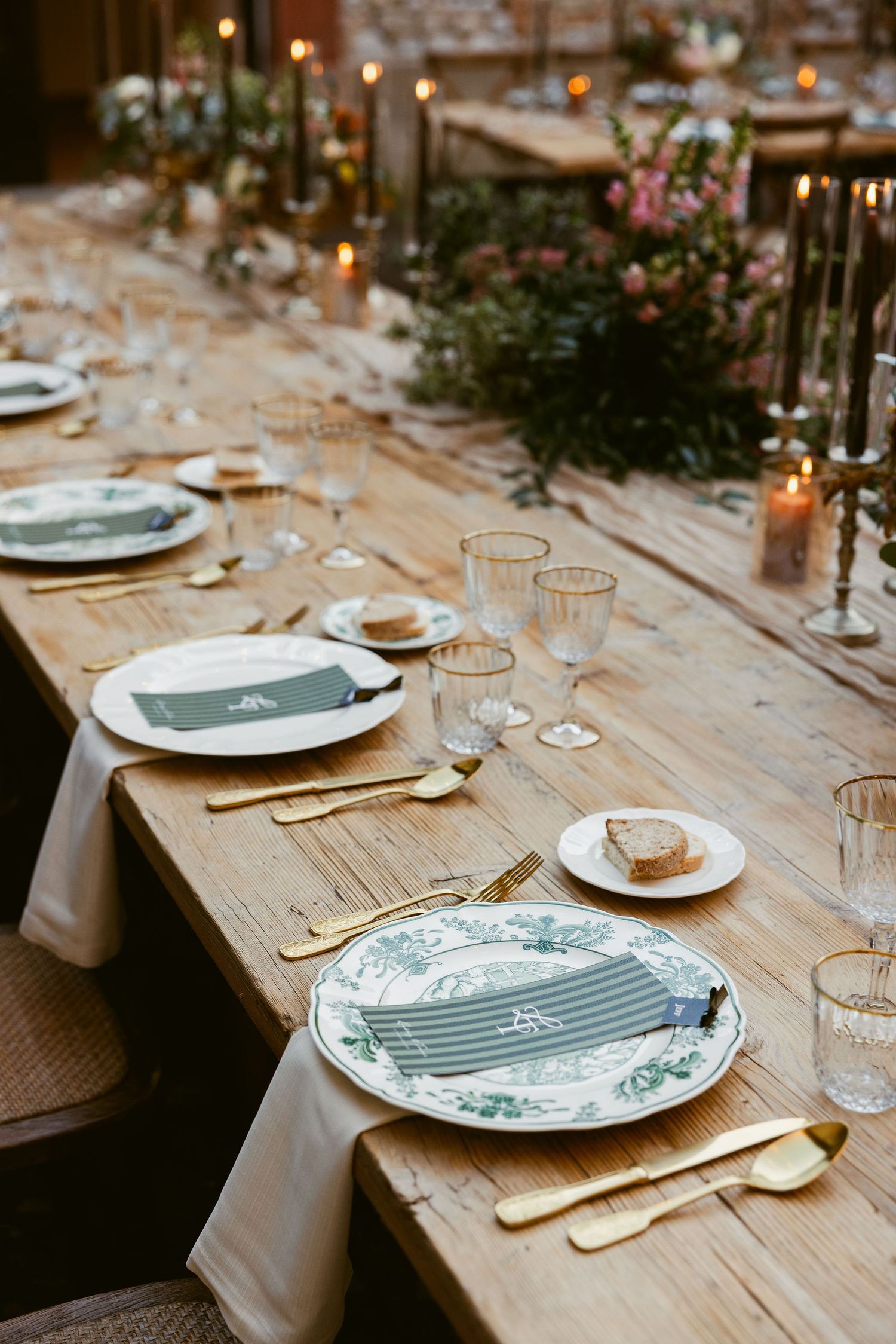 Rustic wooden dining table set with elegant place settings featuring blue and white plates and gold cutlery.