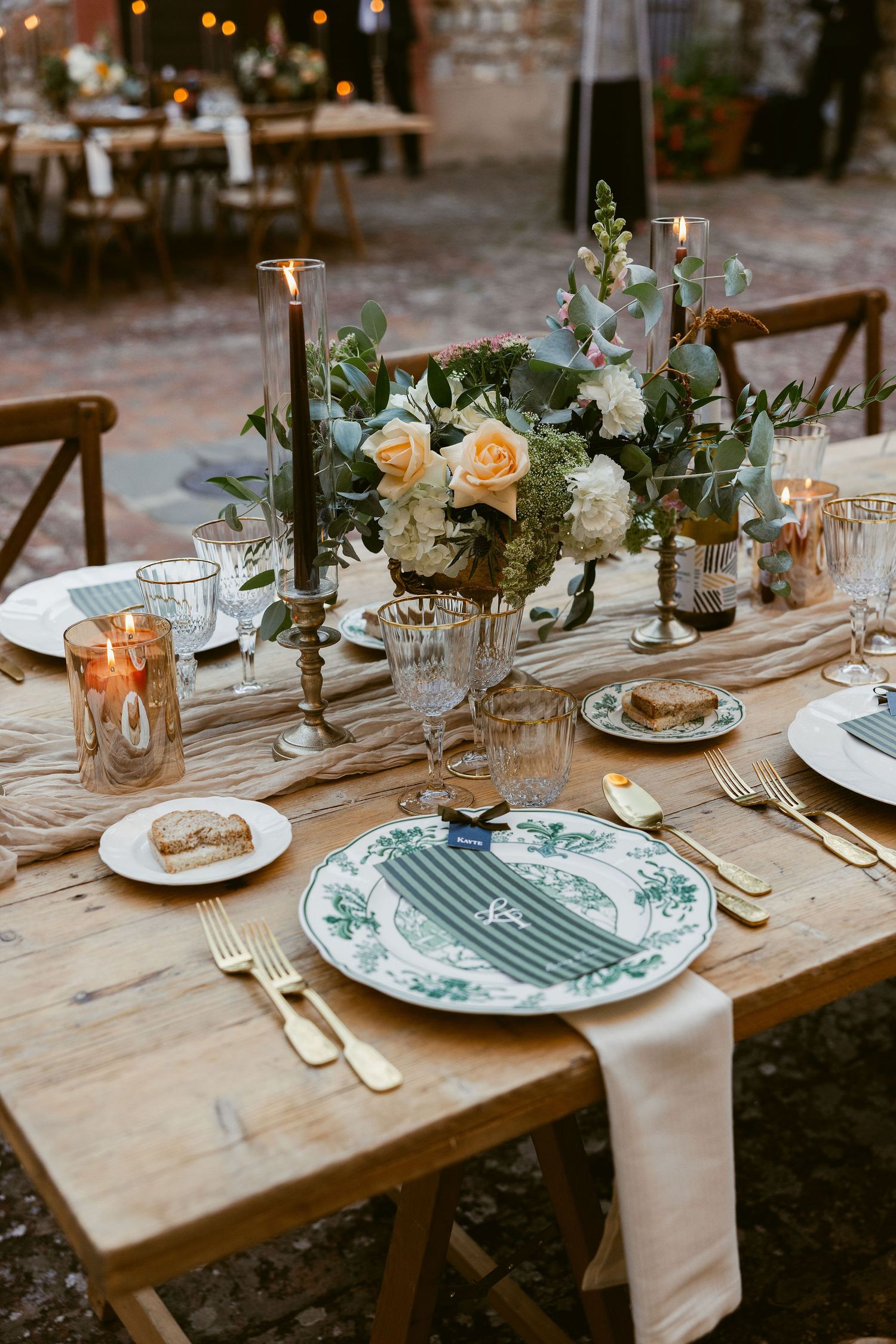 Elegant rustic wedding table setting with vintage plates, peach roses, and greenery on a wooden farm table.