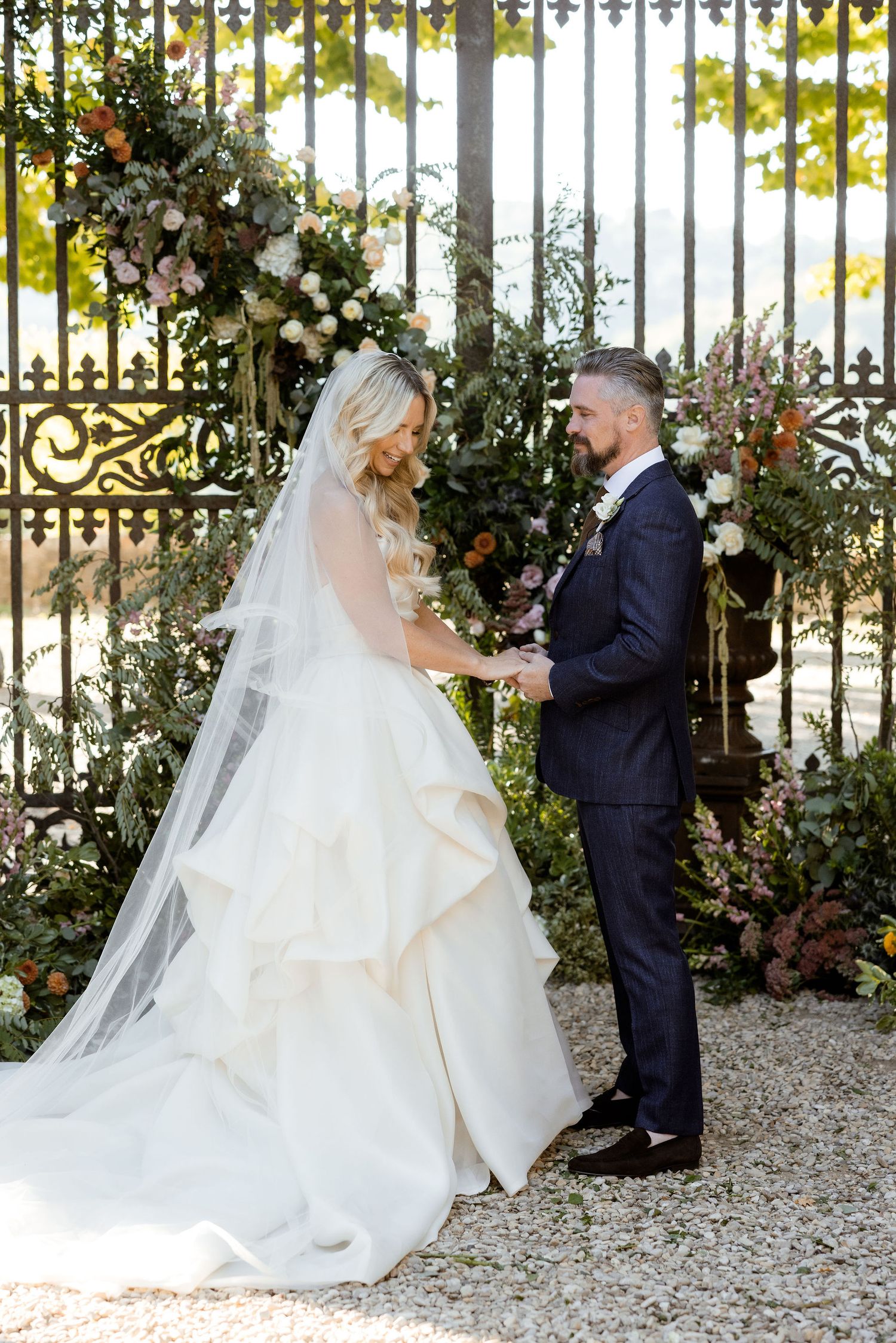 A bride and groom share intimate moments in a garden setting with ornate gates and autumn foliage.