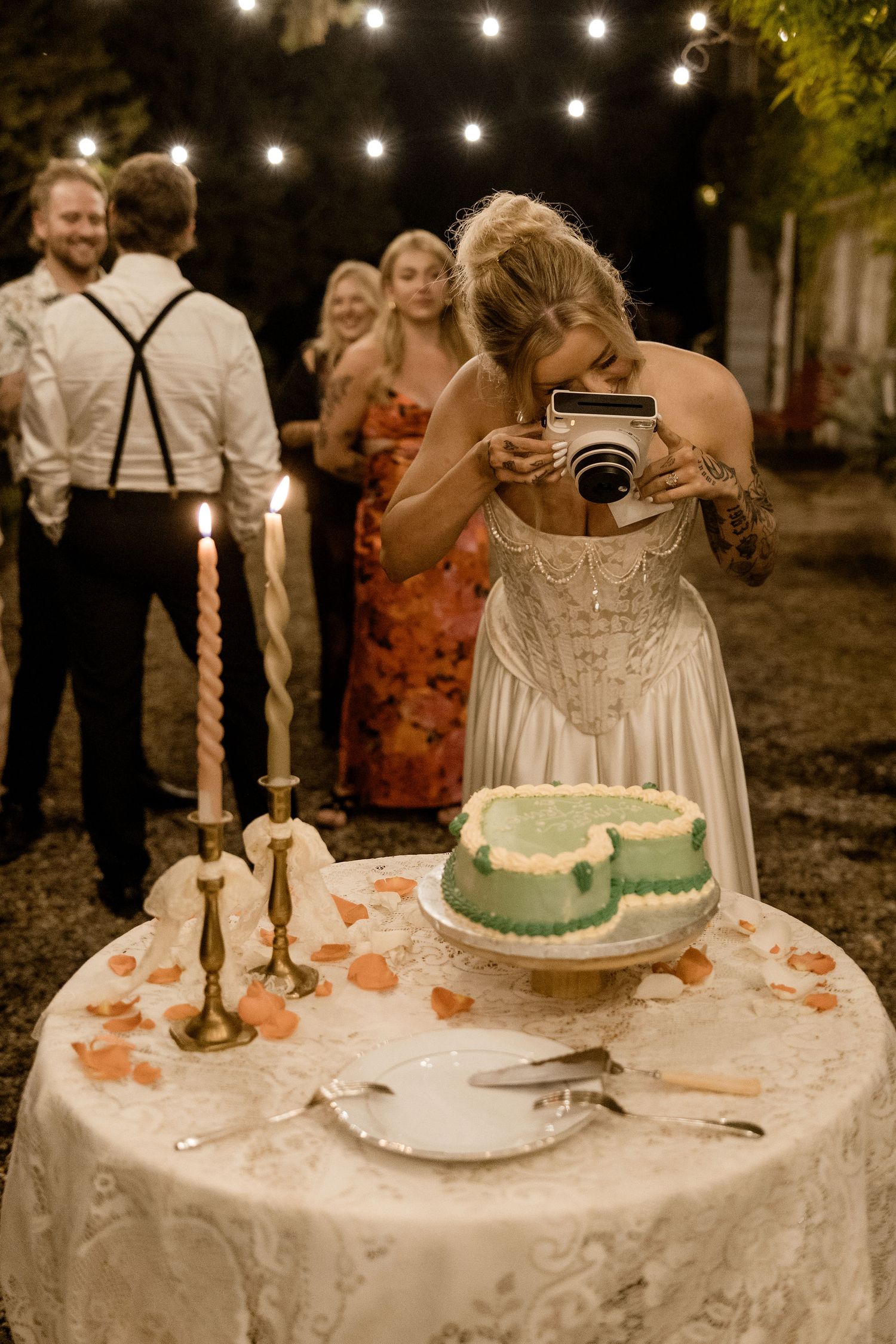 A series of wedding cake photos on a white tablecloth with candlesticks and peach-colored floral decorations at night.