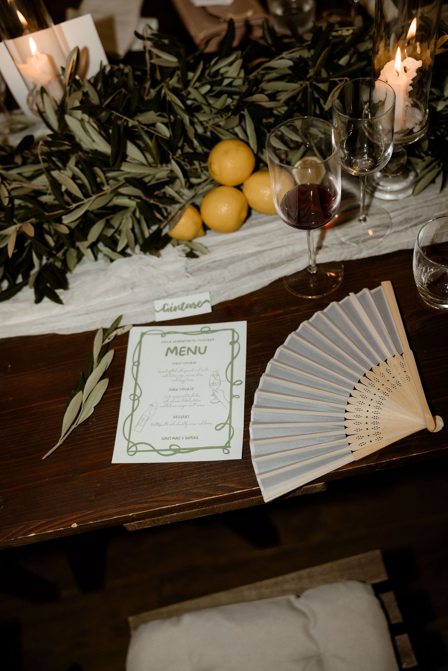 Elegant table decor with paper fans, menu cards, citrus fruits and greenery garlands at a formal dinner setting.