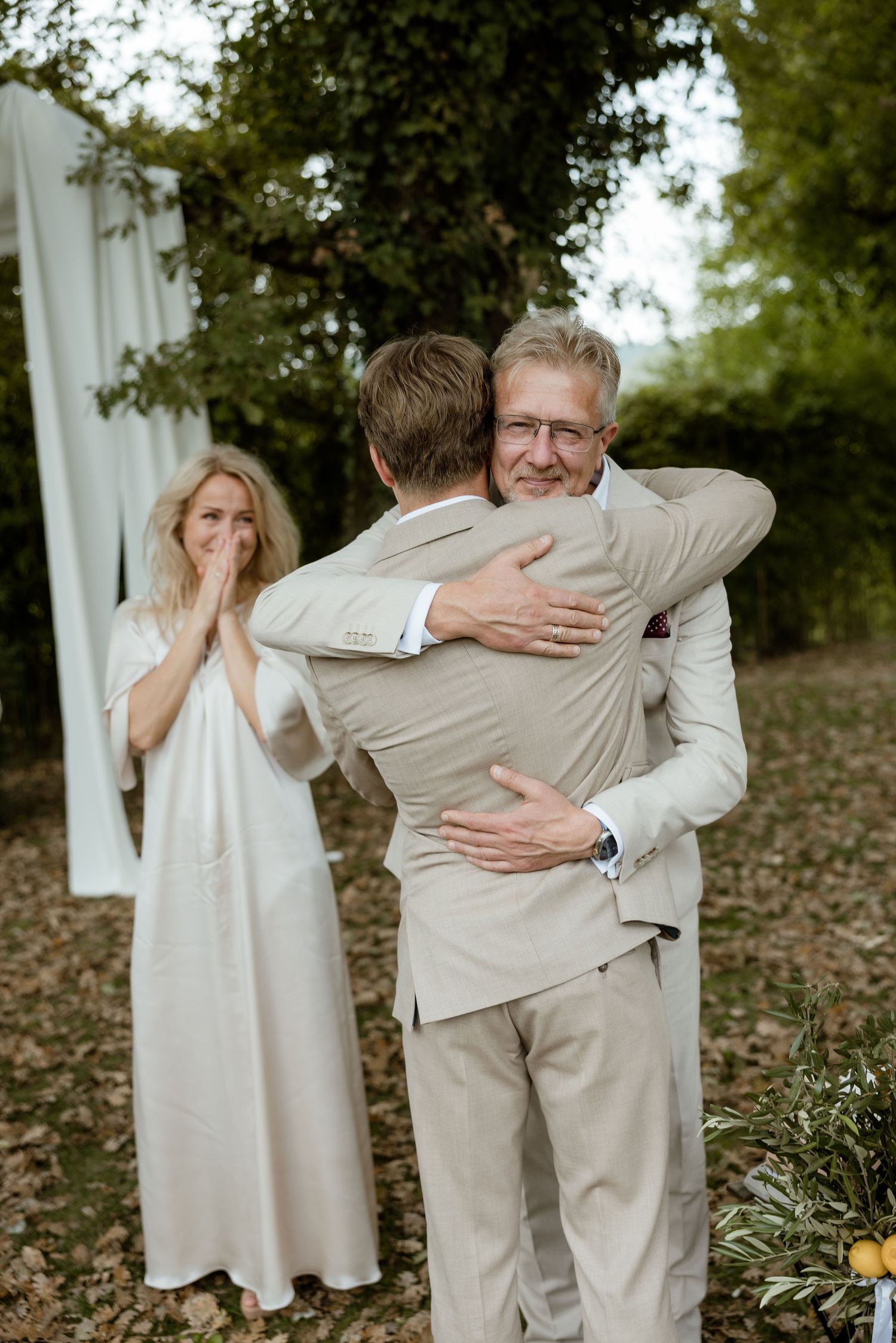 Emotional first look moment between family members embracing outdoors during special occasion.