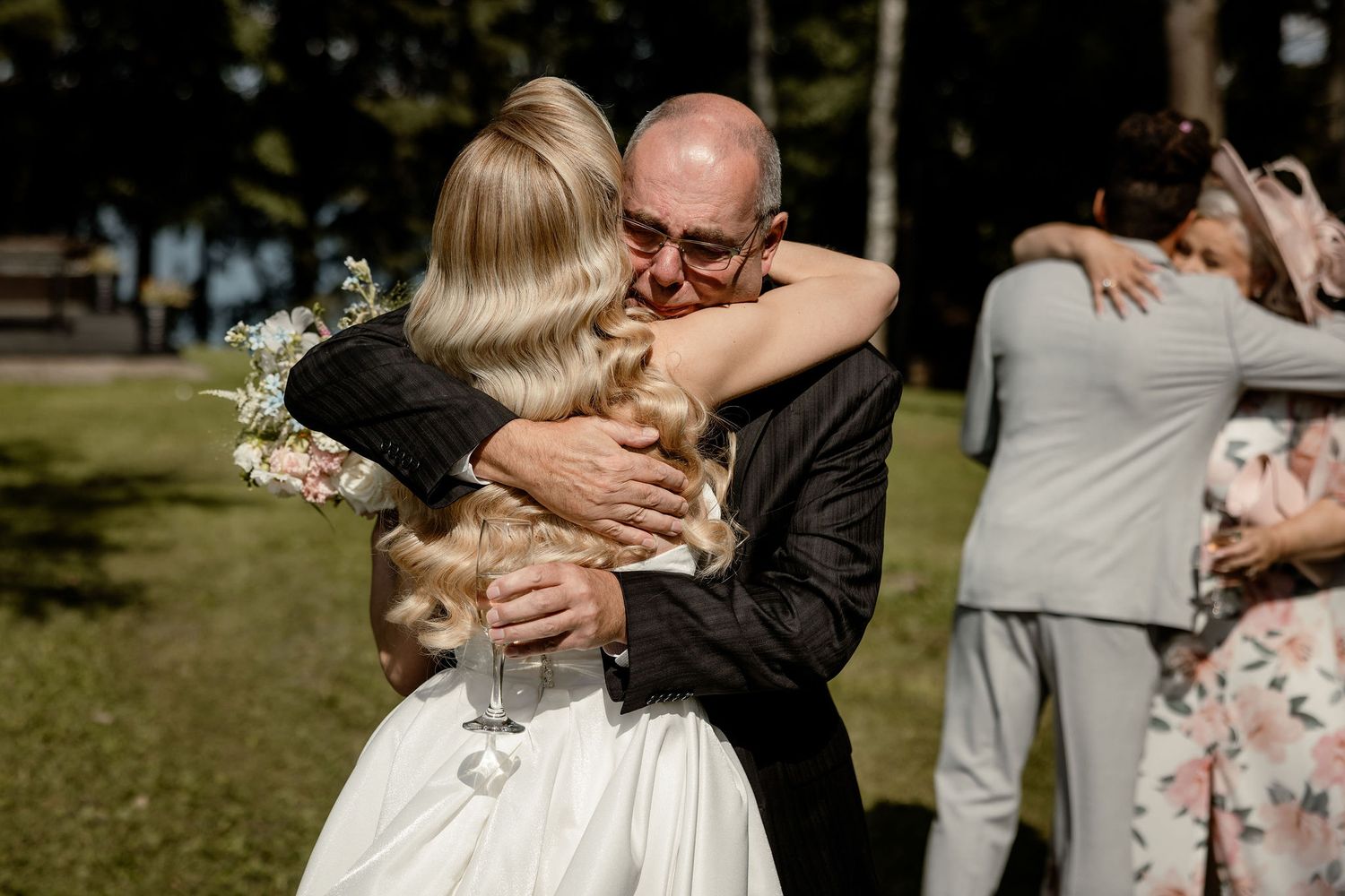 Emotional embrace at an outdoor wedding celebration in a sunny garden setting.