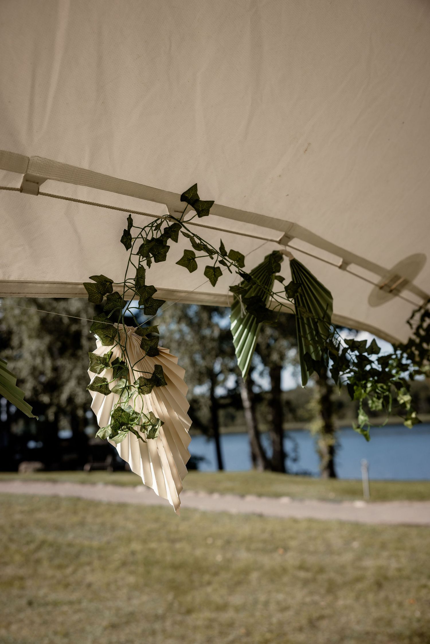 Decorative greenery and white fabric hanging from tent frame with lake view in background.
