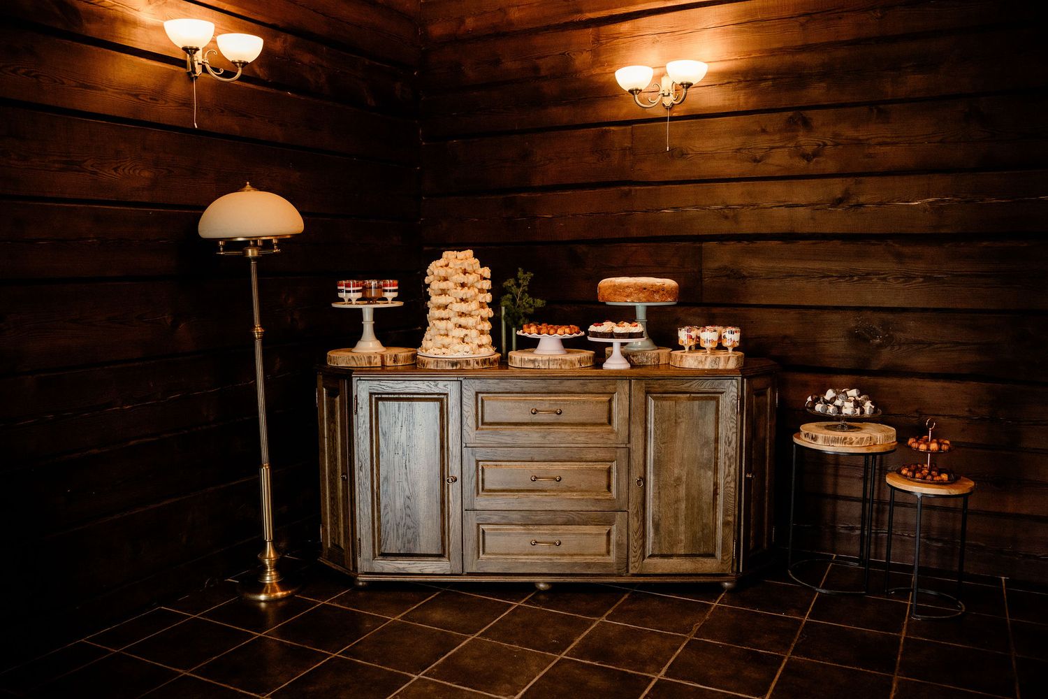 A rustic dessert display table with vintage furniture and warm lighting in a wooden cabin.