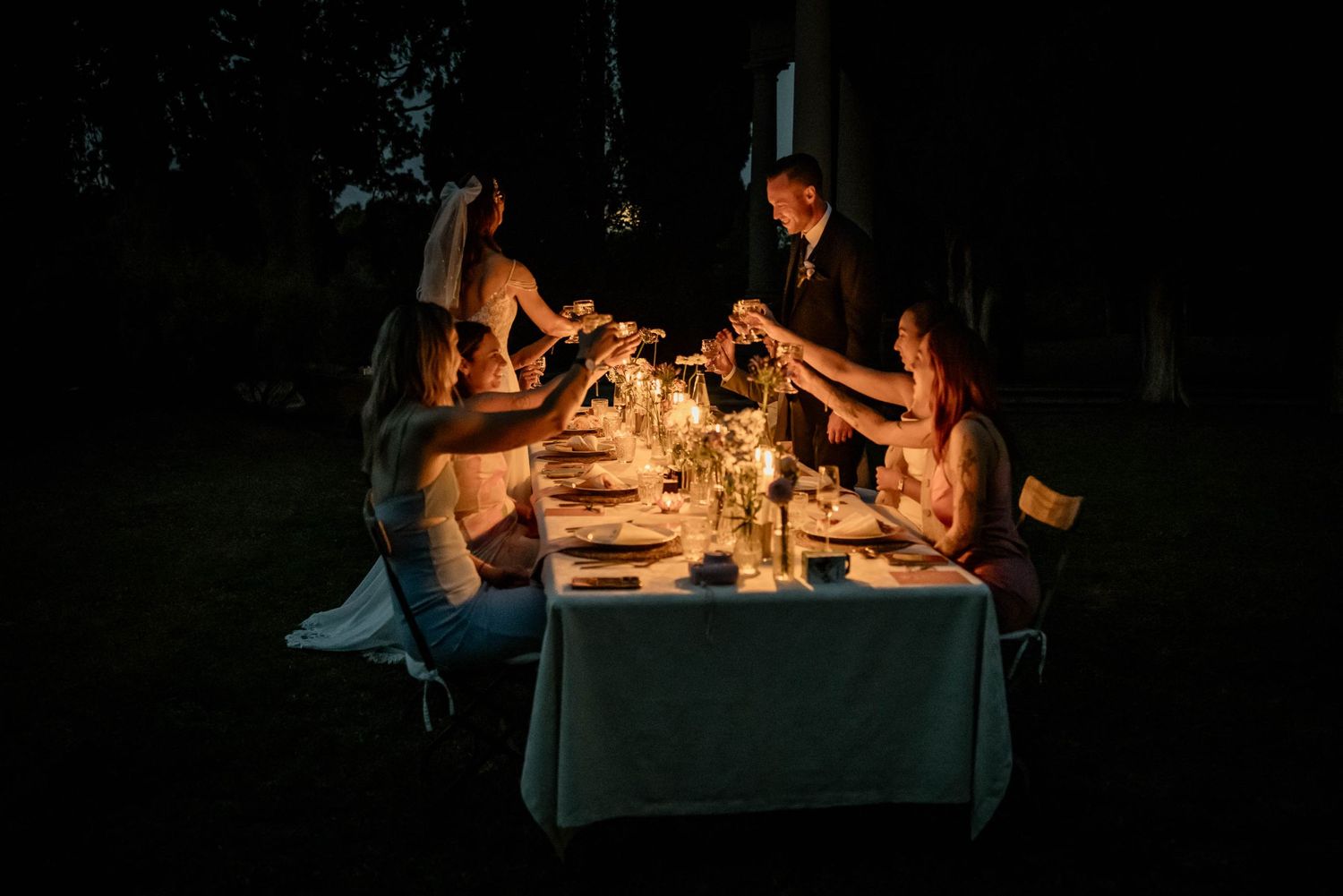 Intimate candlelit outdoor dinner party under string lights at dusk.