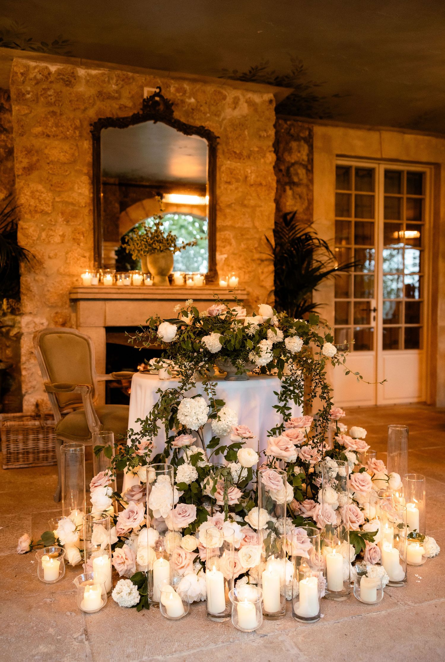 Elegant wedding reception decor with glowing candles and white floral arrangements on stone terrace at dusk.