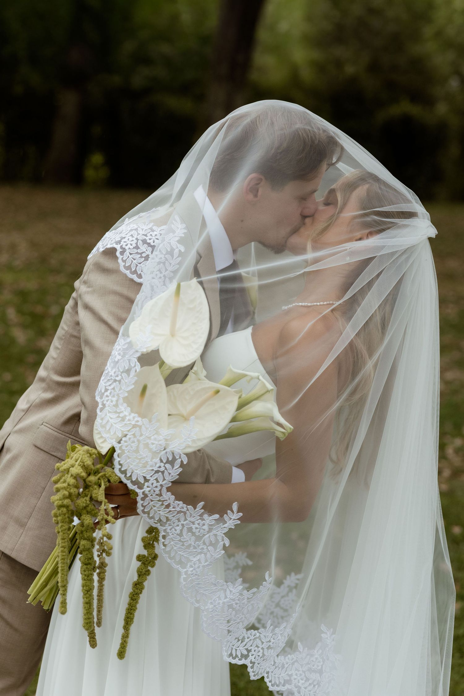 A romantic wedding moment captured through delicate lace veil details and white calla lily bouquet in an outdoor setting.