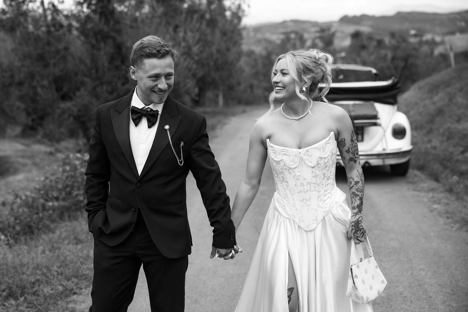 A couple in formal wedding attire walking together on a country road in black and white.