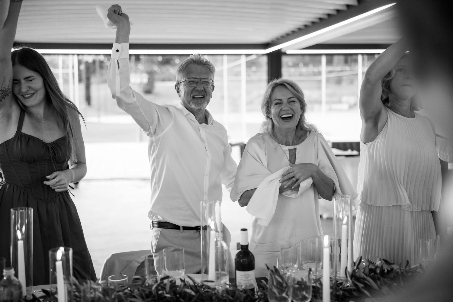 A joyful black and white candid moment of celebration at a party with people laughing and raising their hands.