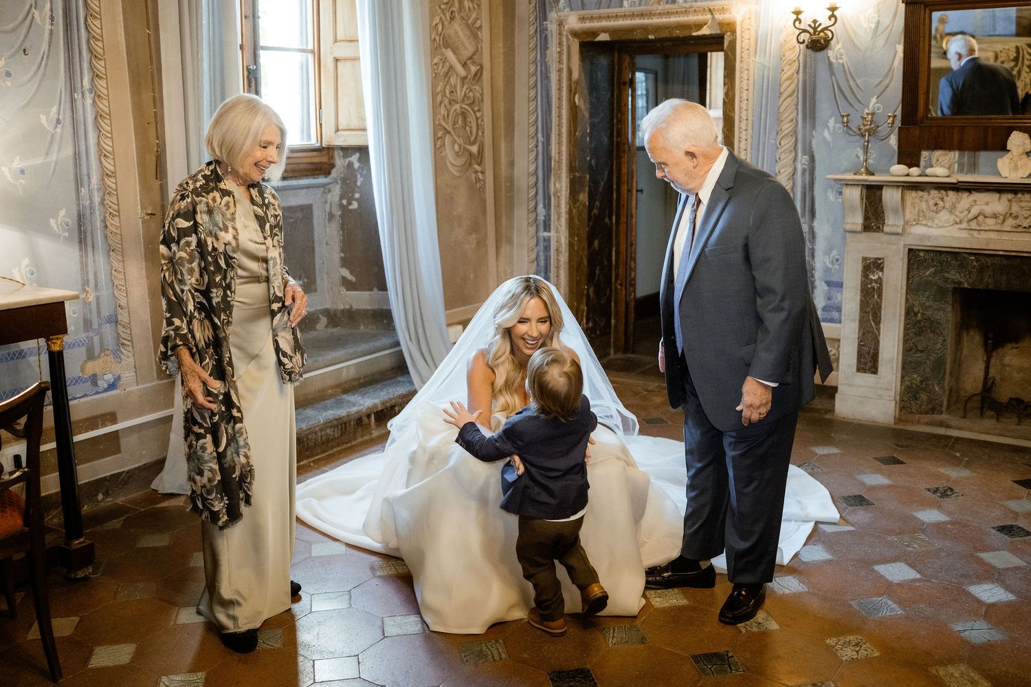 People in formal attire gather in an ornate room with elegant decor and traditional furnishings.