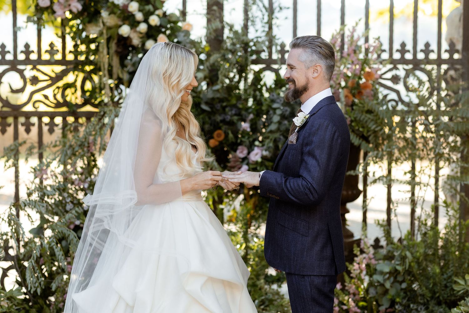 A bride and groom share a romantic moment together in a garden setting surrounded by ornate iron gates.