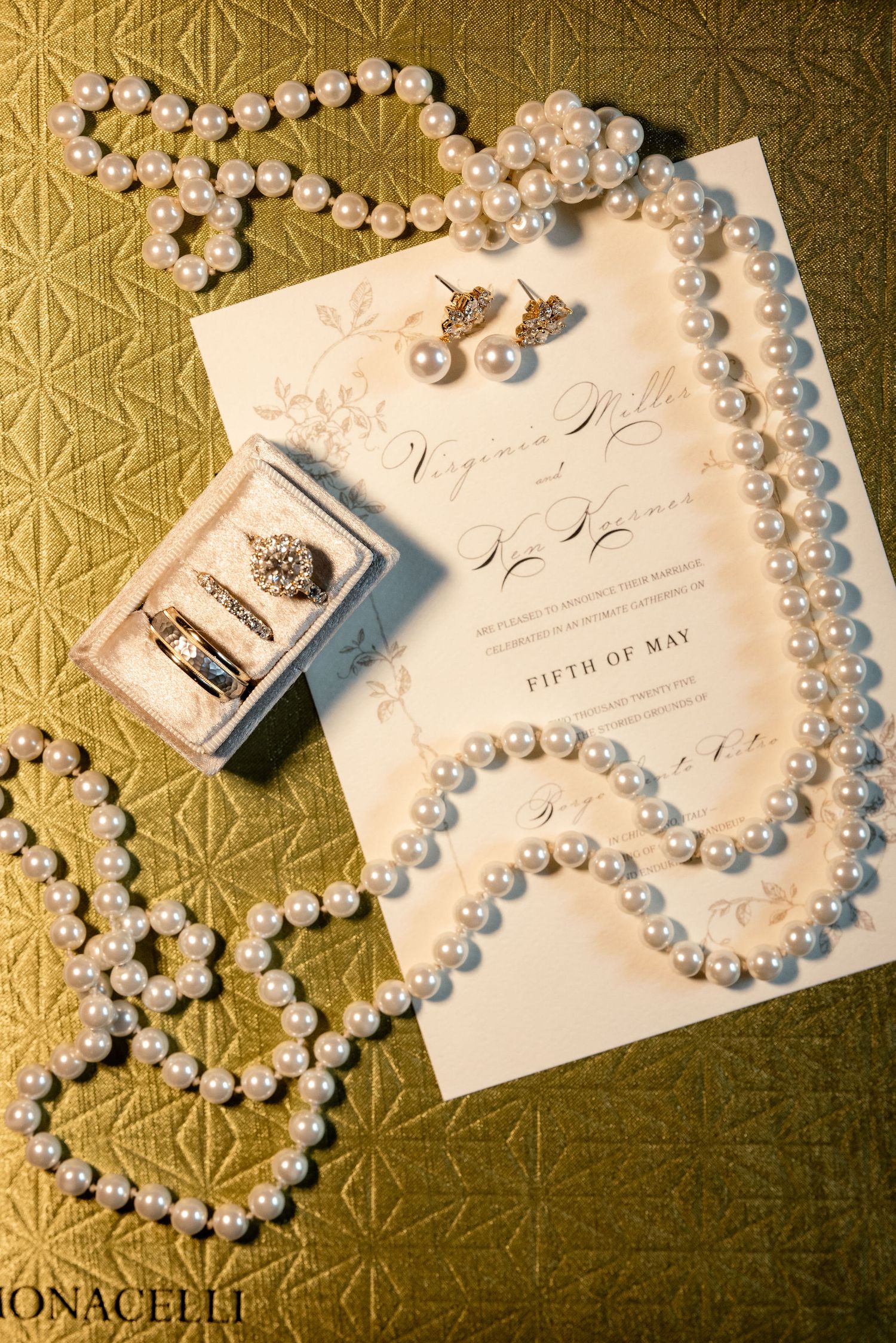 Elegant wedding invitation with pearl necklace, earrings and vintage photo on textured gold background.