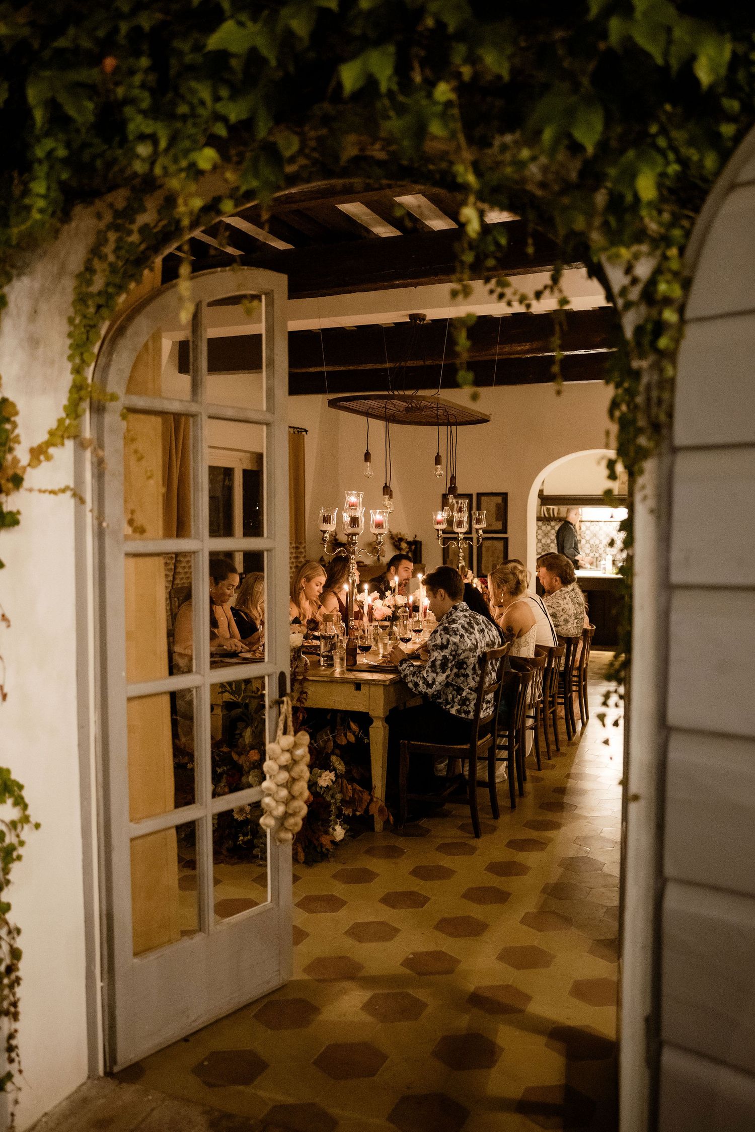 Elegant wedding reception venue with hanging greenery and chandeliers illuminating long dining tables.