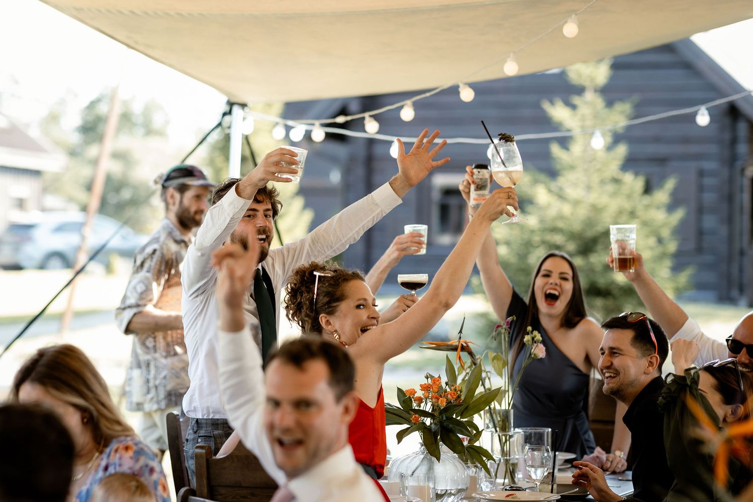 Outdoor celebration with guests raising glasses in a toast under string lights.